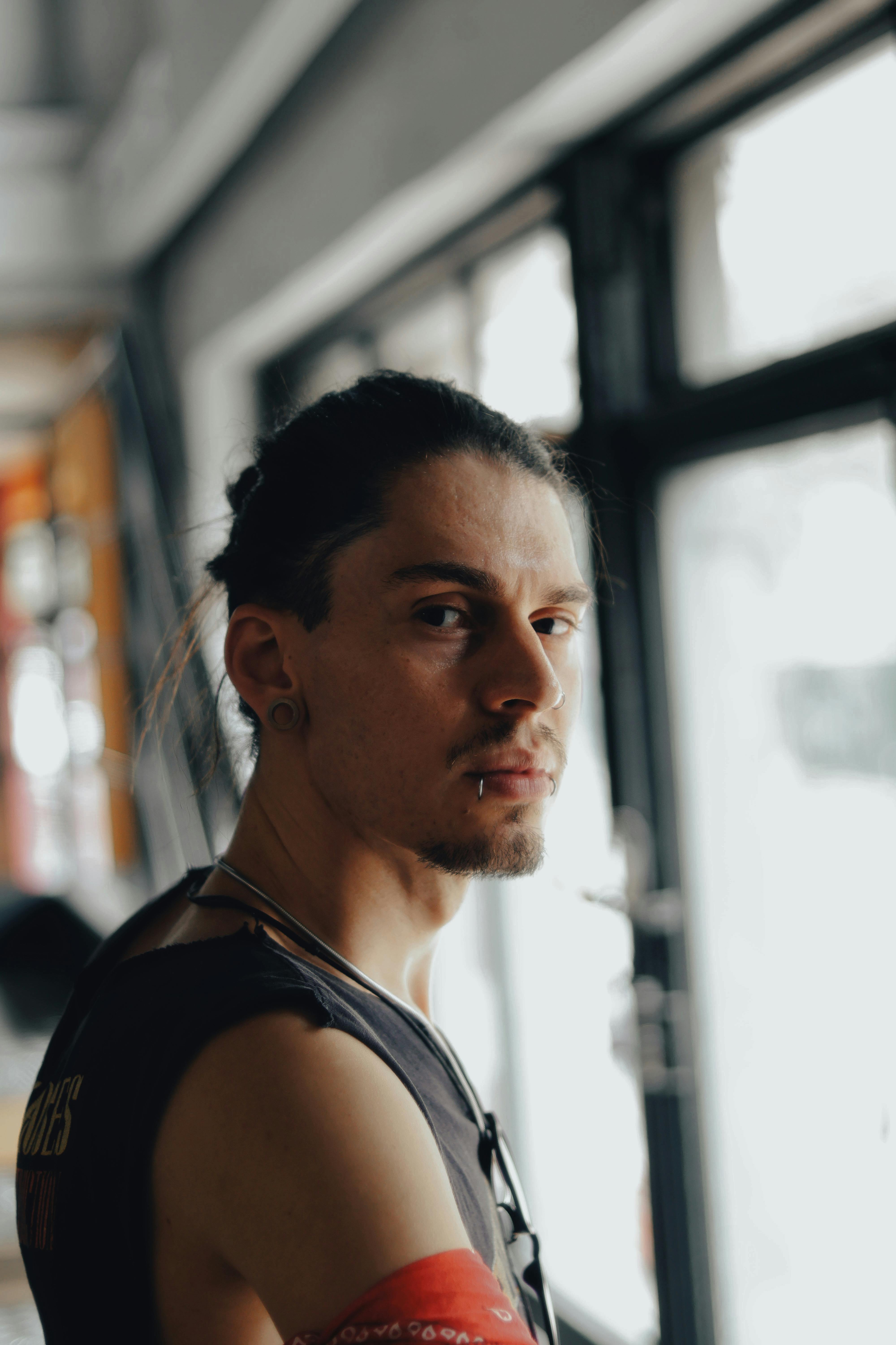 Kostenlos Ein nachdenklicher junger Mann mit Piercings in einem Innenraum, der in die Kamera schaut. Stock-Foto