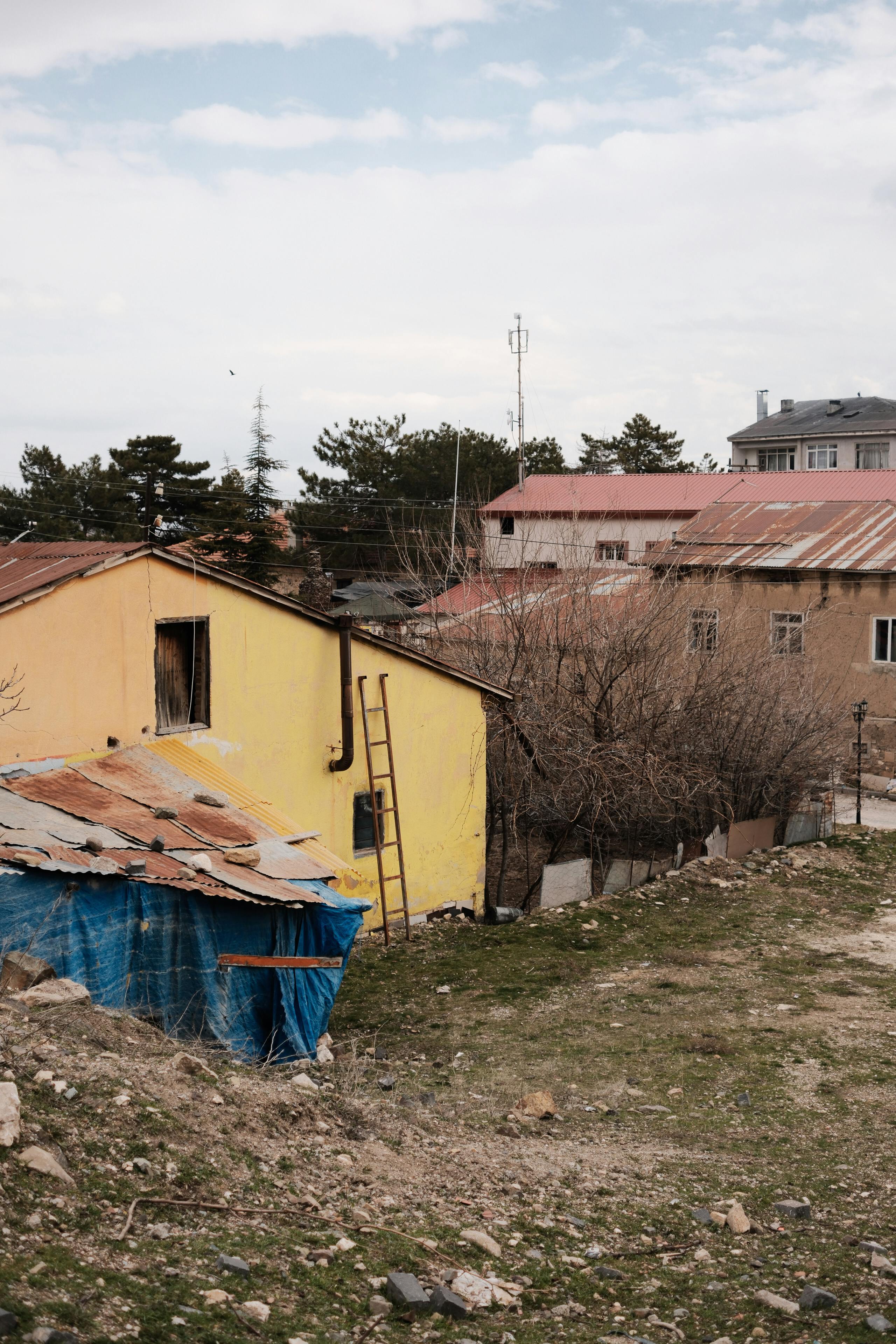 Kostenlos Ländliche Szenerie mit leuchtend gelben und braunen Häusern inmitten kahler Bäume und unbefestigtem Gelände. Stock-Foto