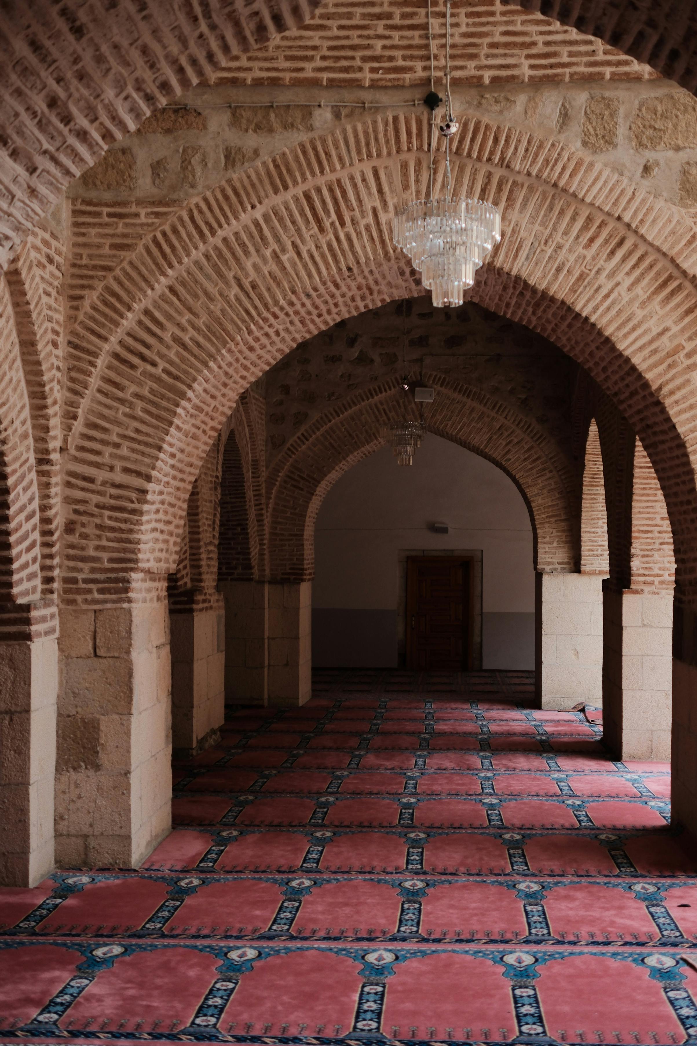 Kostenlos Ein wunderschön gemusterter Teppich säumt einen historischen Bogengang mit aufwendiger Backsteinarchitektur. Stock-Foto