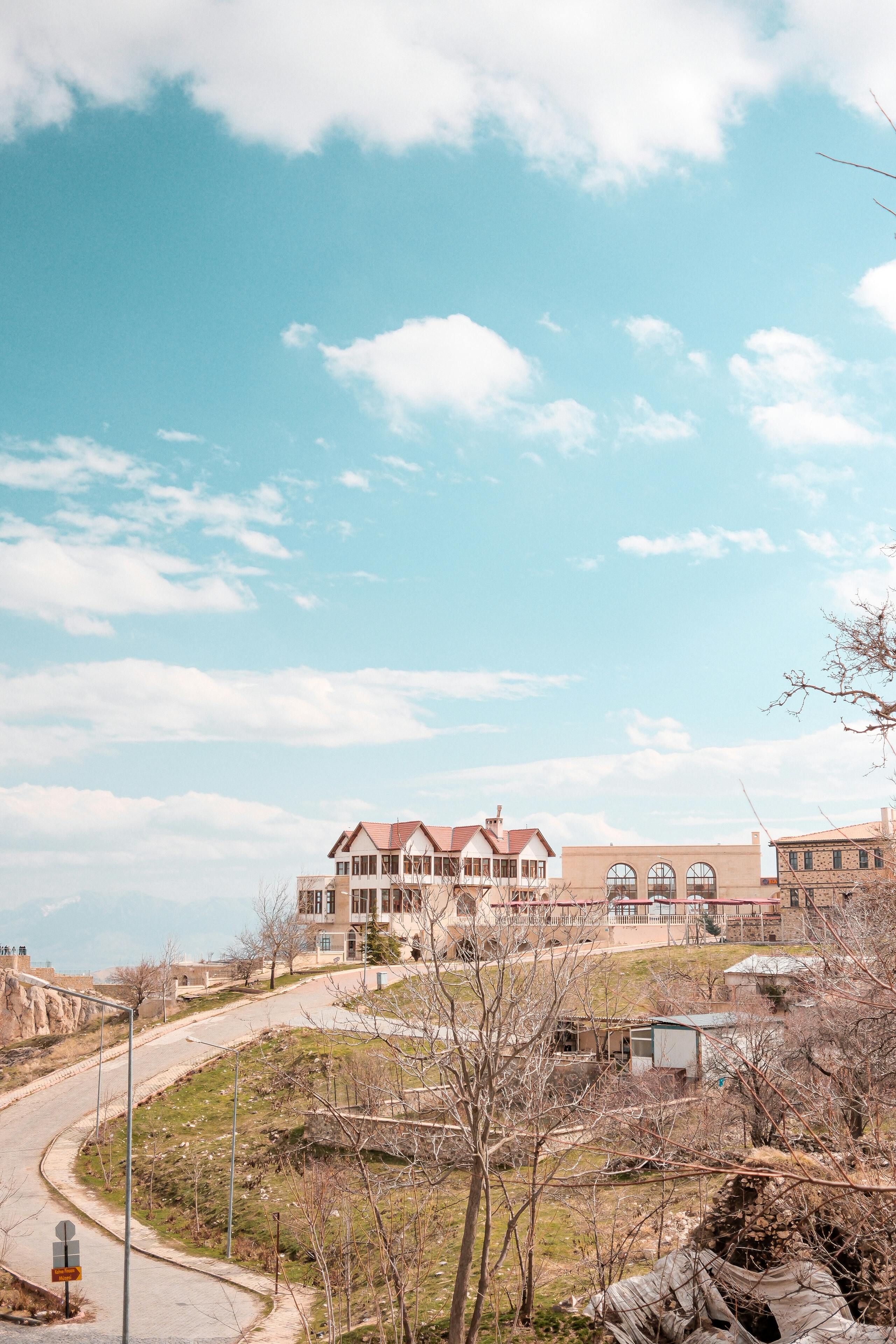 Kostenlos Malerische Ansicht eines Hauses auf einem Hügel mit einer Straße und klarem blauen Himmel, aufgenommen bei Tageslicht. Stock-Foto