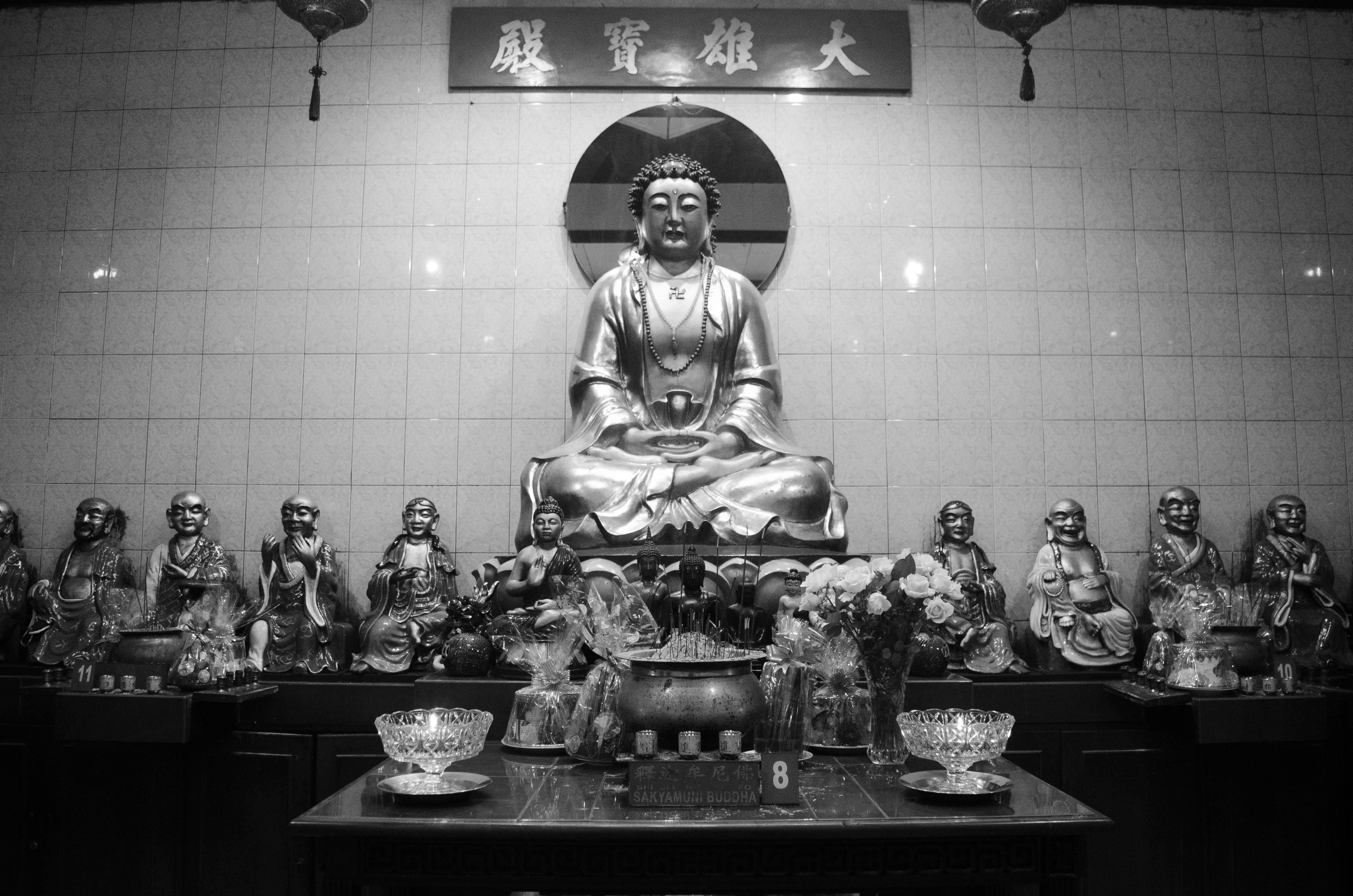 Kostenlos Schwarz-Weiß-Fotografie einer friedvollen Buddha-Statue, umgeben von kleineren Figuren in einem friedlichen Schrein. Stock-Foto