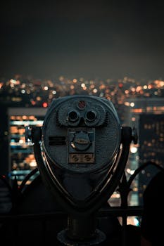 Telescope overlooks New York City skyline at night, capturing stunning urban lights.