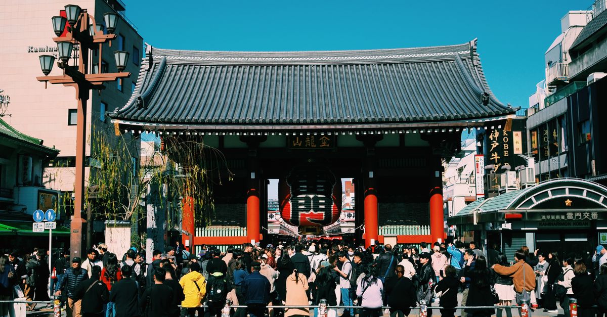 Large crowd gathers at the iconic Senso-ji Temple gate in Tokyo, Japan, under a clear blue sky.