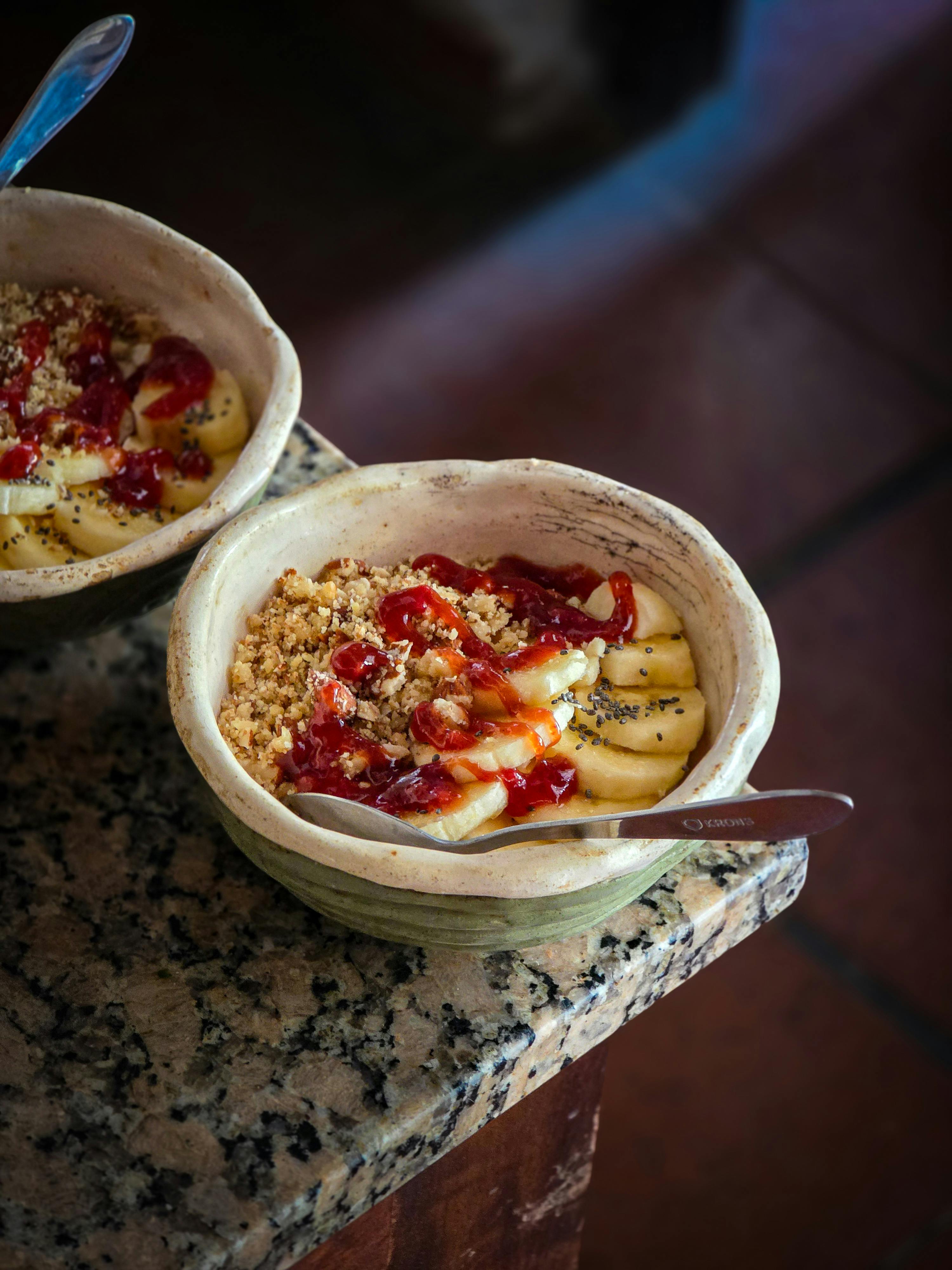 Kostenlos Nahaufnahme von Frühstücksschalen mit Bananen, Müsli und Marmelade auf einer rustikalen Oberfläche. Stock-Foto