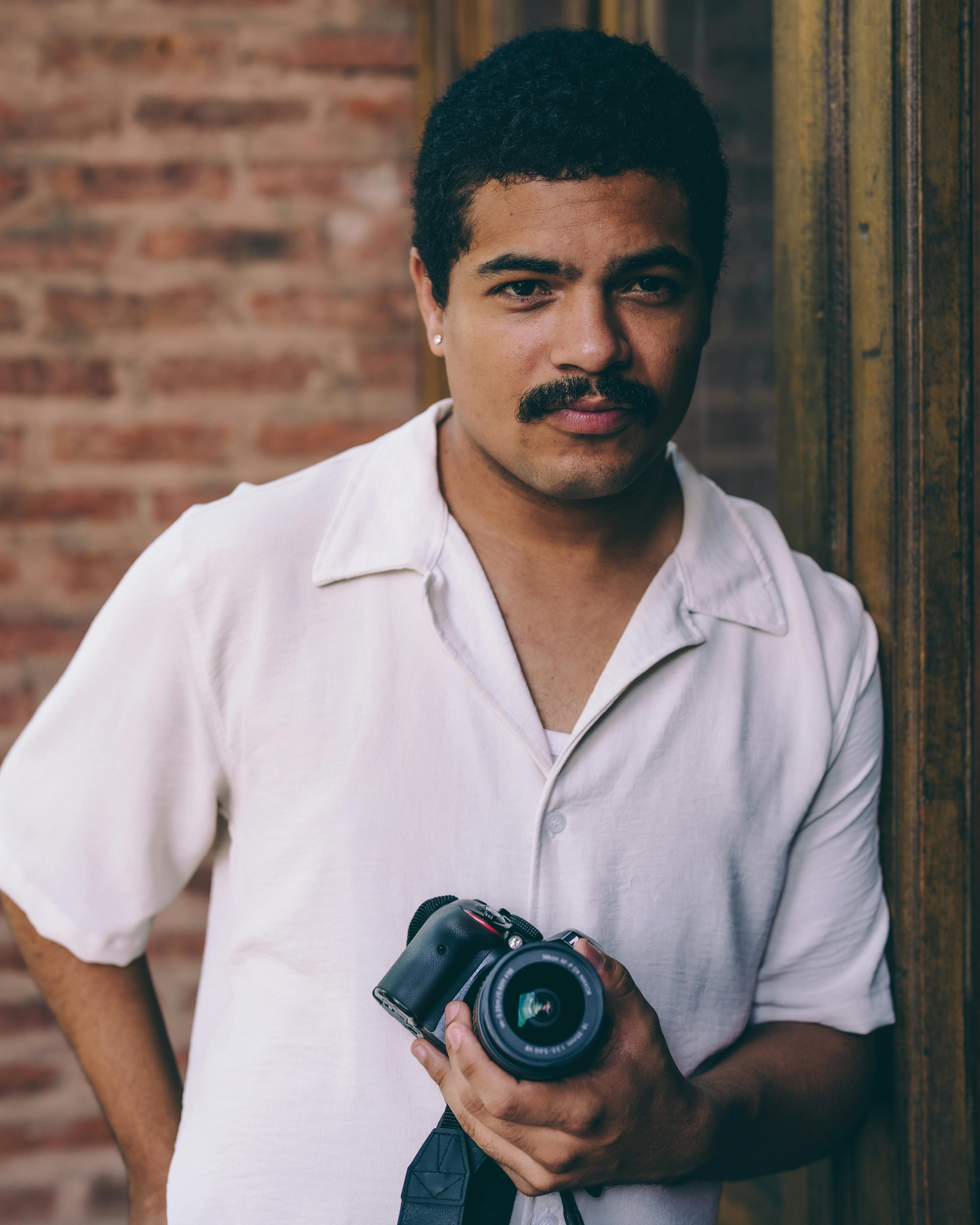 Kostenlos Stilvolles Porträt eines Fotografen, der eine Vintage-Kamera an eine Backsteinmauer hält. Stock-Foto