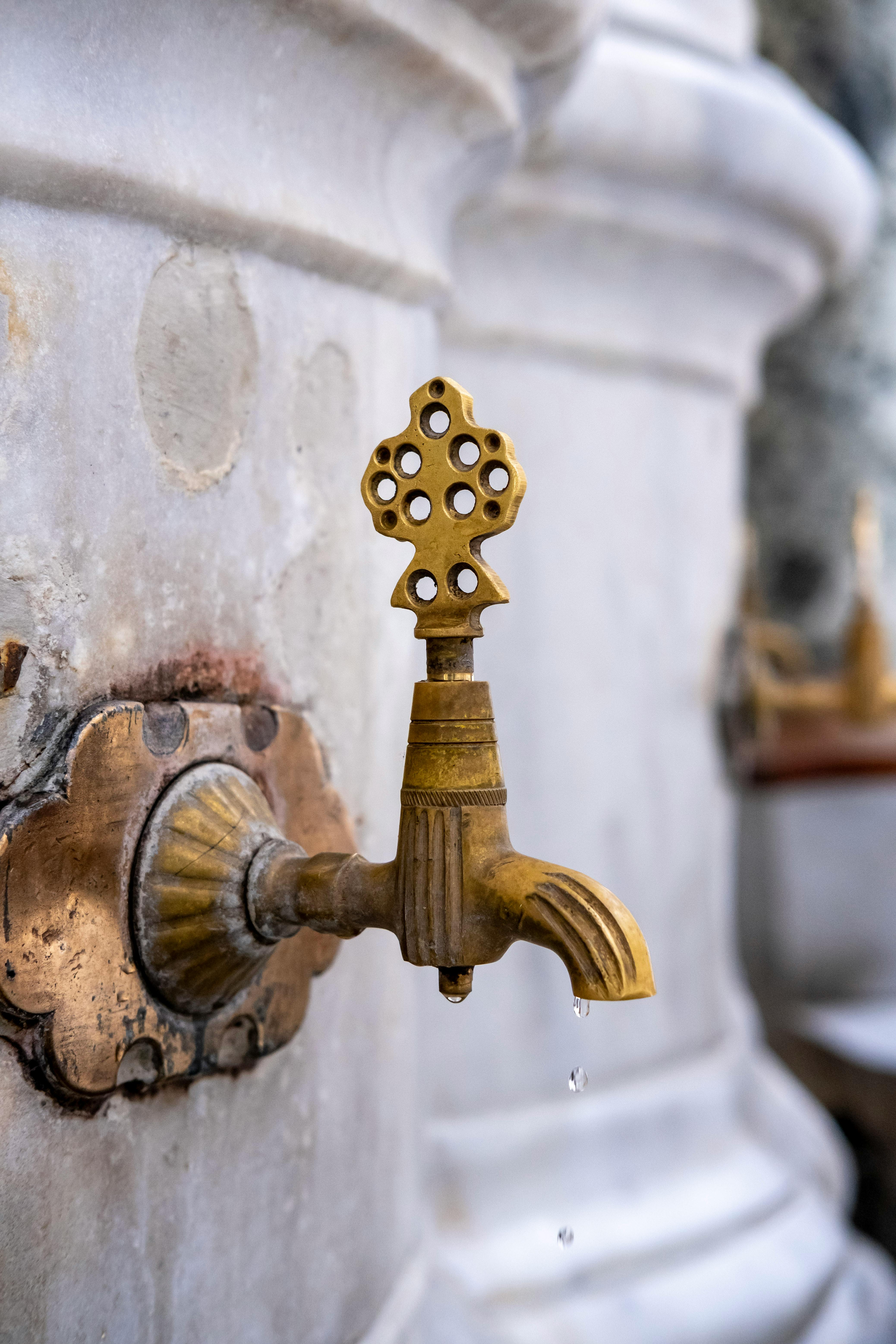 Kostenlos Nahaufnahme eines reich verzierten Messinghahns mit dekorativem Muster auf einem Marmorbrunnen. Stock-Foto