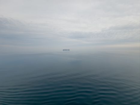Calm ocean view with a distant cargo ship under a cloudy sky.