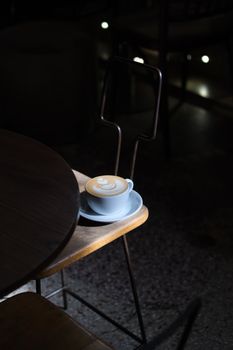 Artistic presentation of a cafe latte with a leaf pattern on a chair in dim lighting.