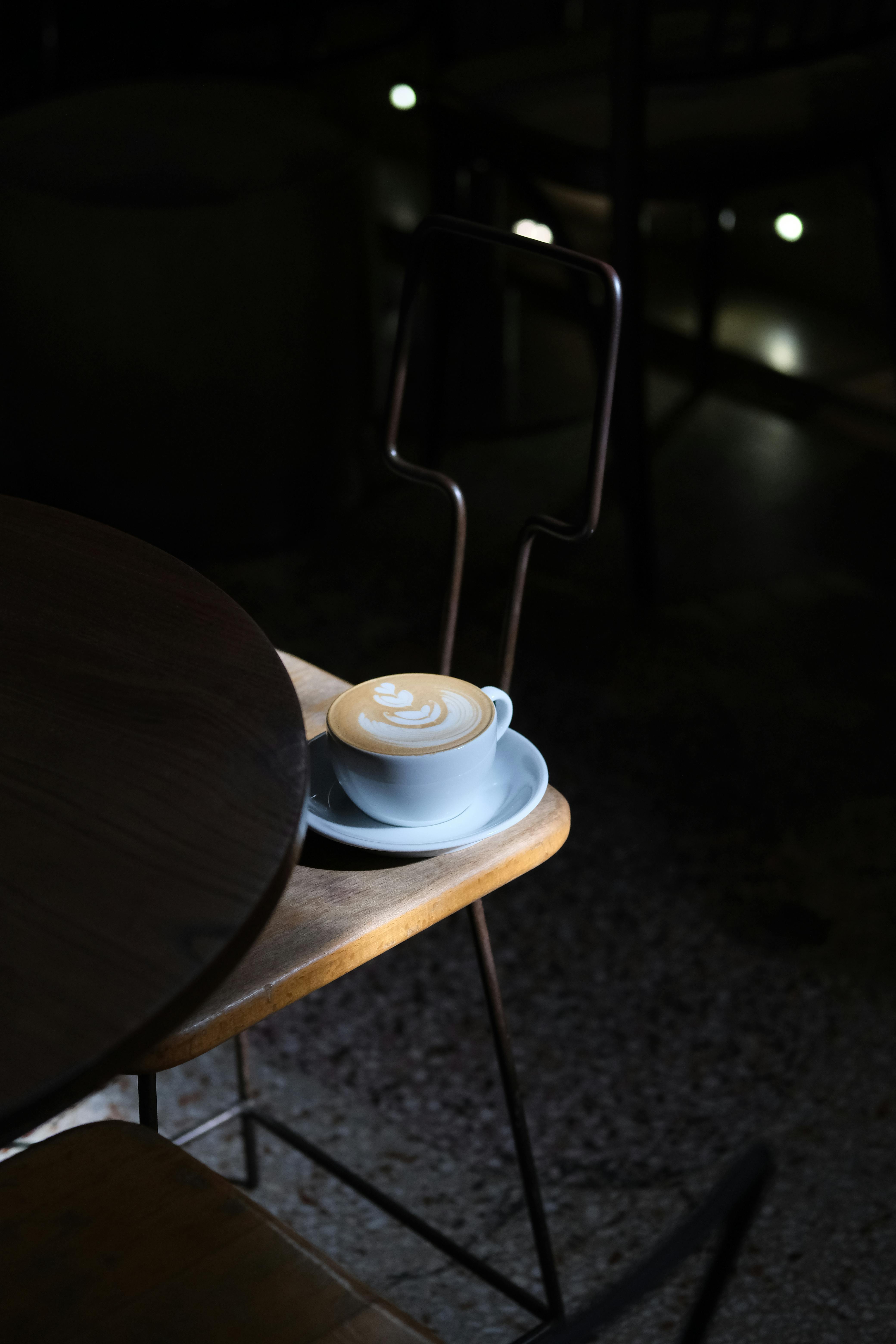 Free Artistic presentation of a cafe latte with a leaf pattern on a chair in dim lighting. Stock Photo