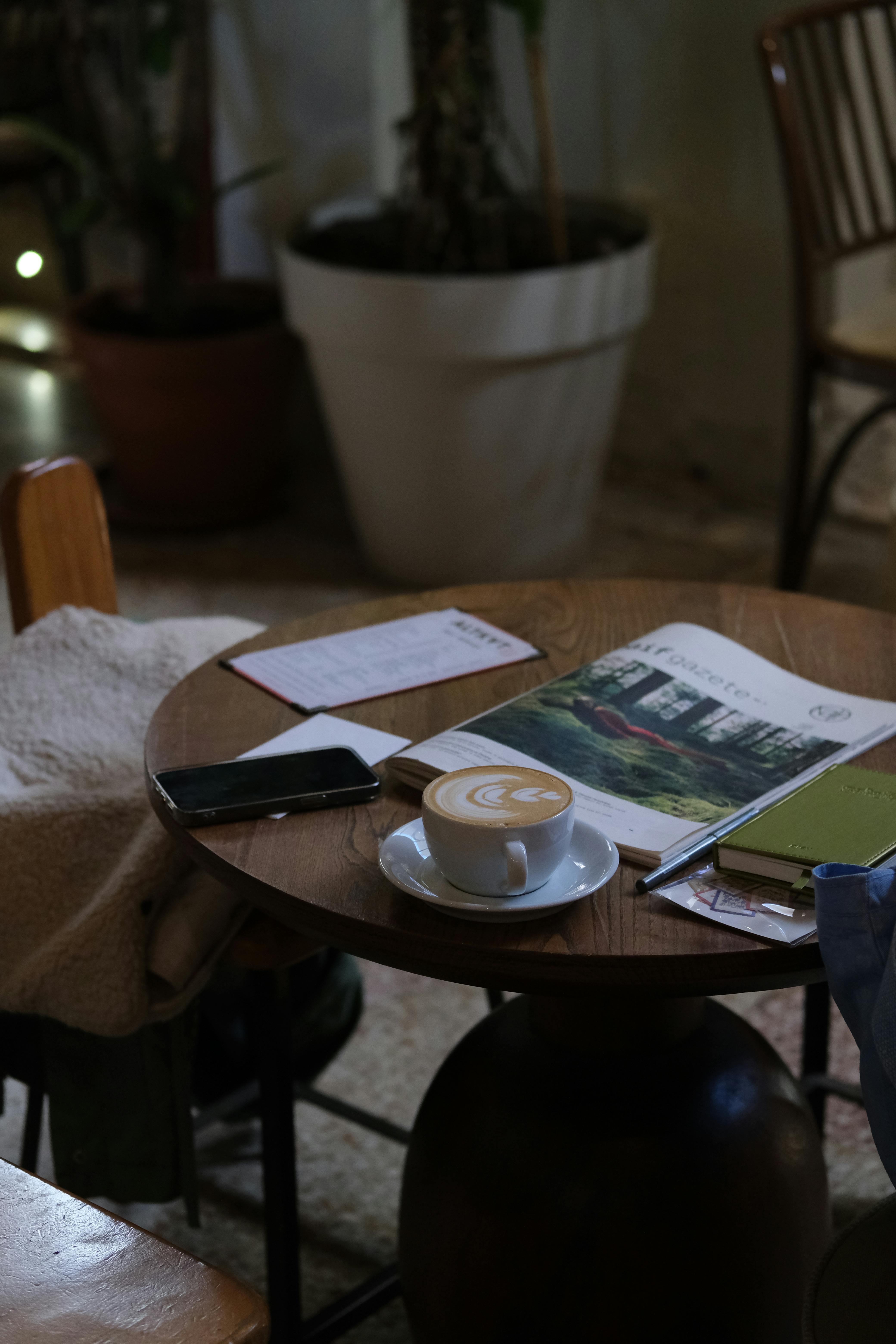 Δωρεάν Ένα ζεστό σκηνικό καφέ με λάτε και περιοδικά σε ένα ρουστίκ τραπέζι, ιδανικό για χαλάρωση. Φωτογραφία από στοκ φωτογραφιών