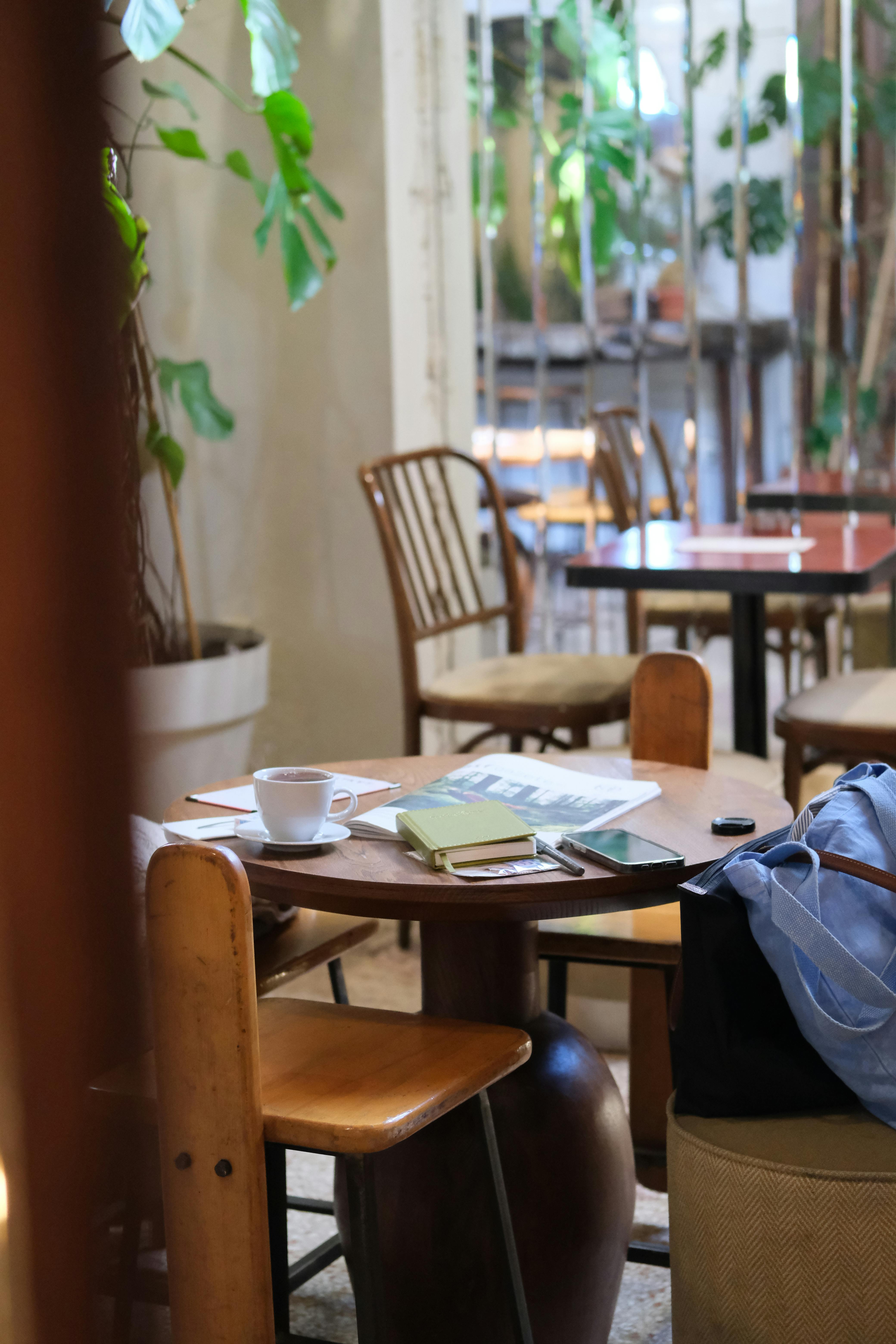Gratis En stille caféscene med et bord med notesbøger, kaffe og afslappede siddepladser. Lagerfoto