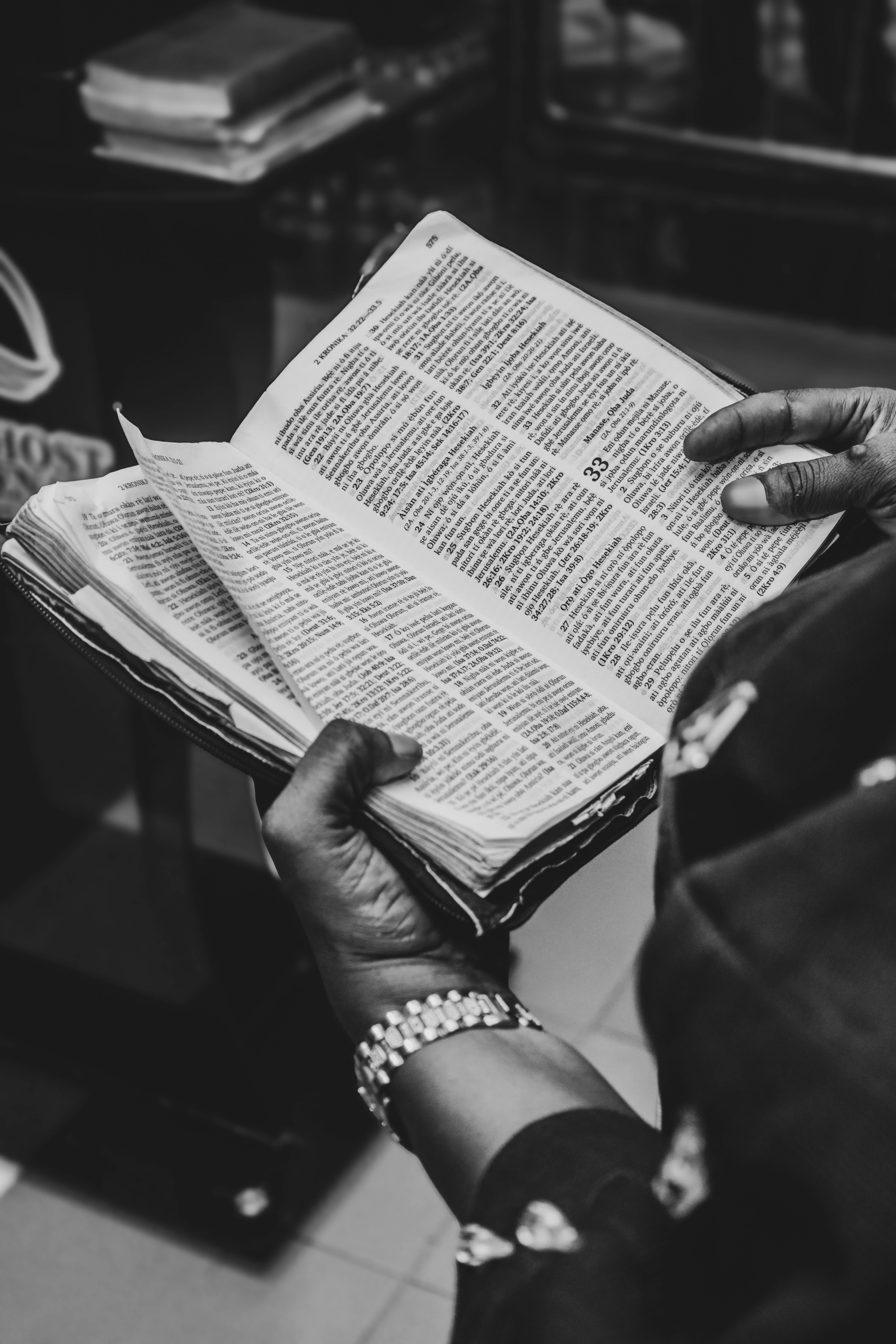 Kostenlos Schwarzweißfoto eines Erwachsenen, der ein aufgeschlagenes Buch hält und den Blick auf den detaillierten Text richtet. Stock-Foto