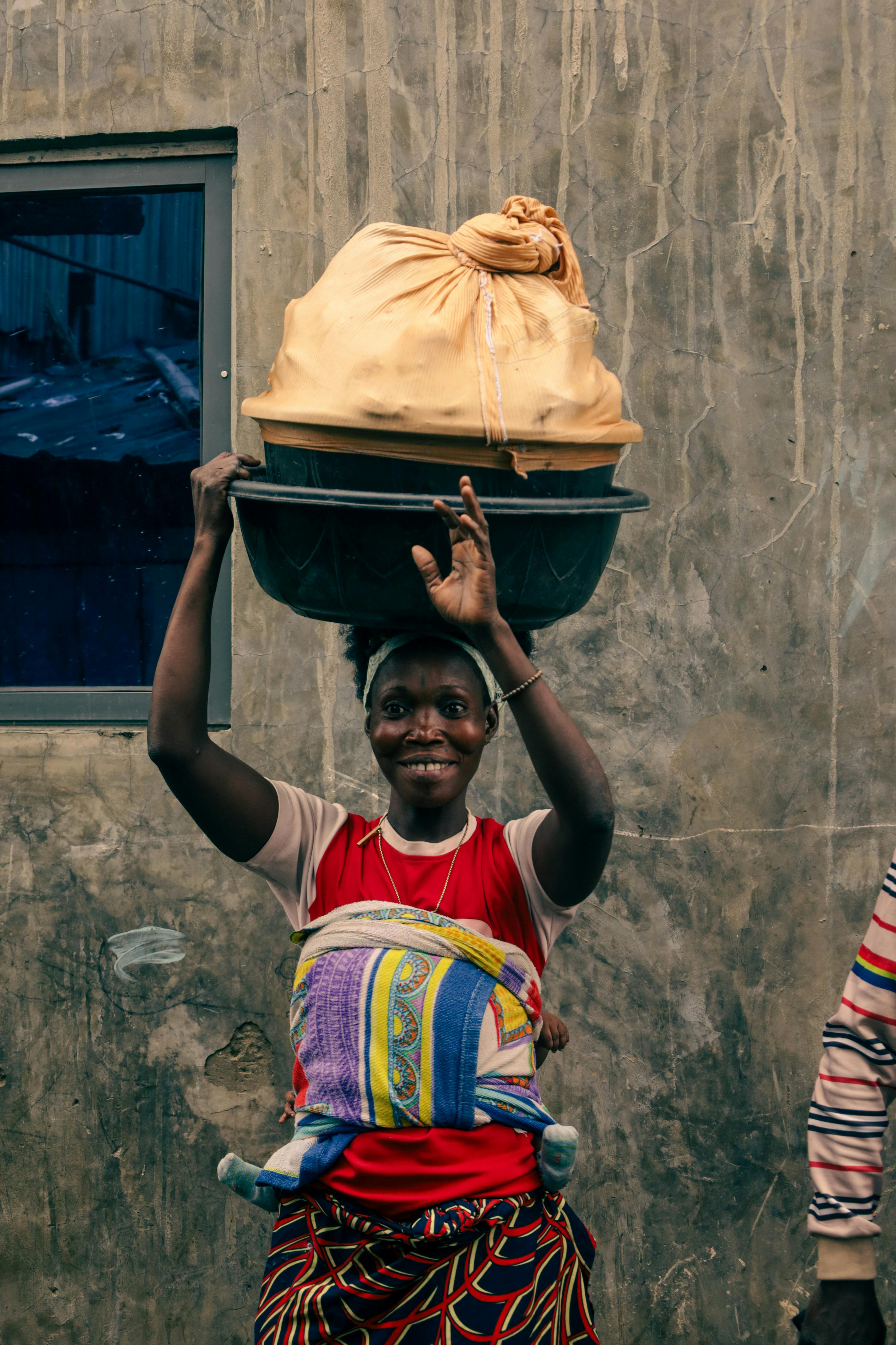 Kostenlos Eine lächelnde Frau trägt einen Korb auf dem Kopf und präsentiert damit die afrikanische Kultur. Stock-Foto