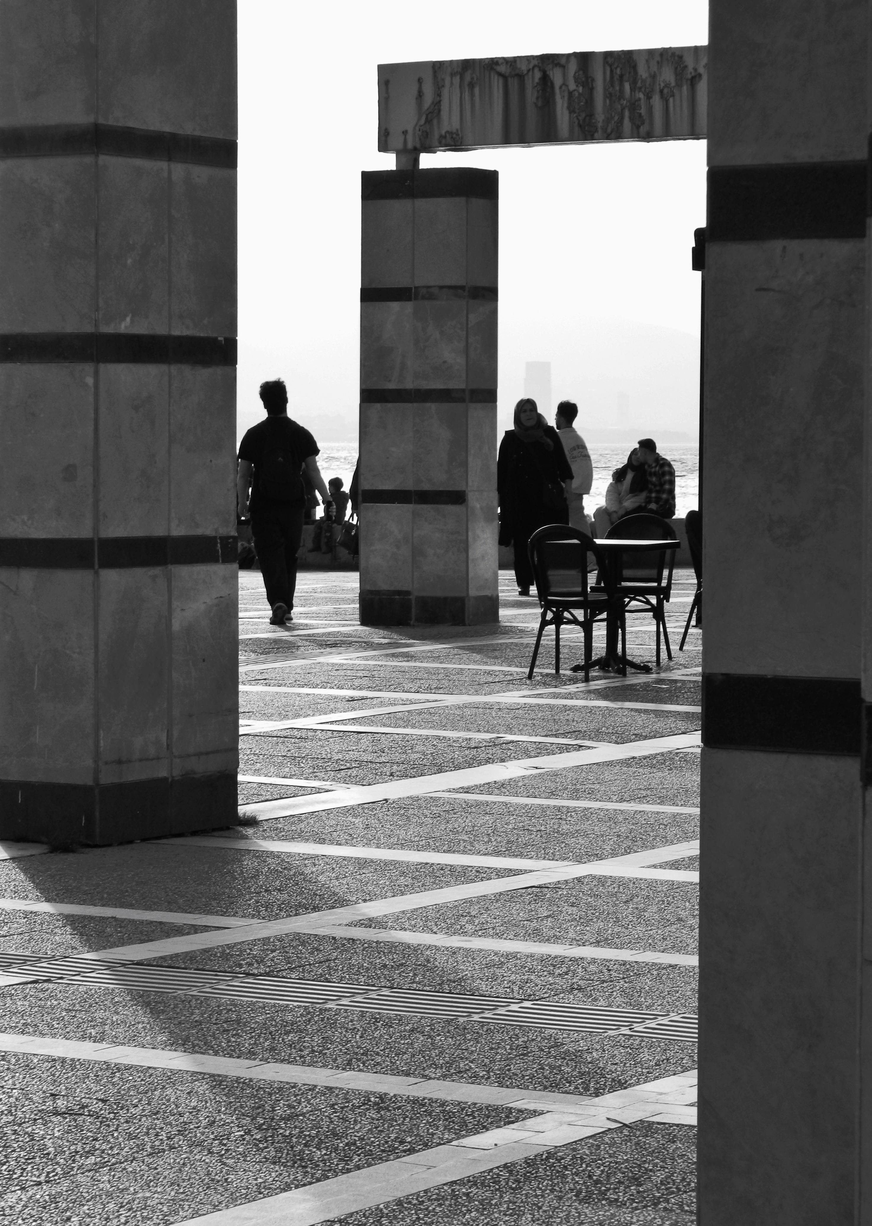 бесплатная Черно-белый городской пейзаж, на котором люди проходят мимо больших колонн и стульев. Стоковое фото