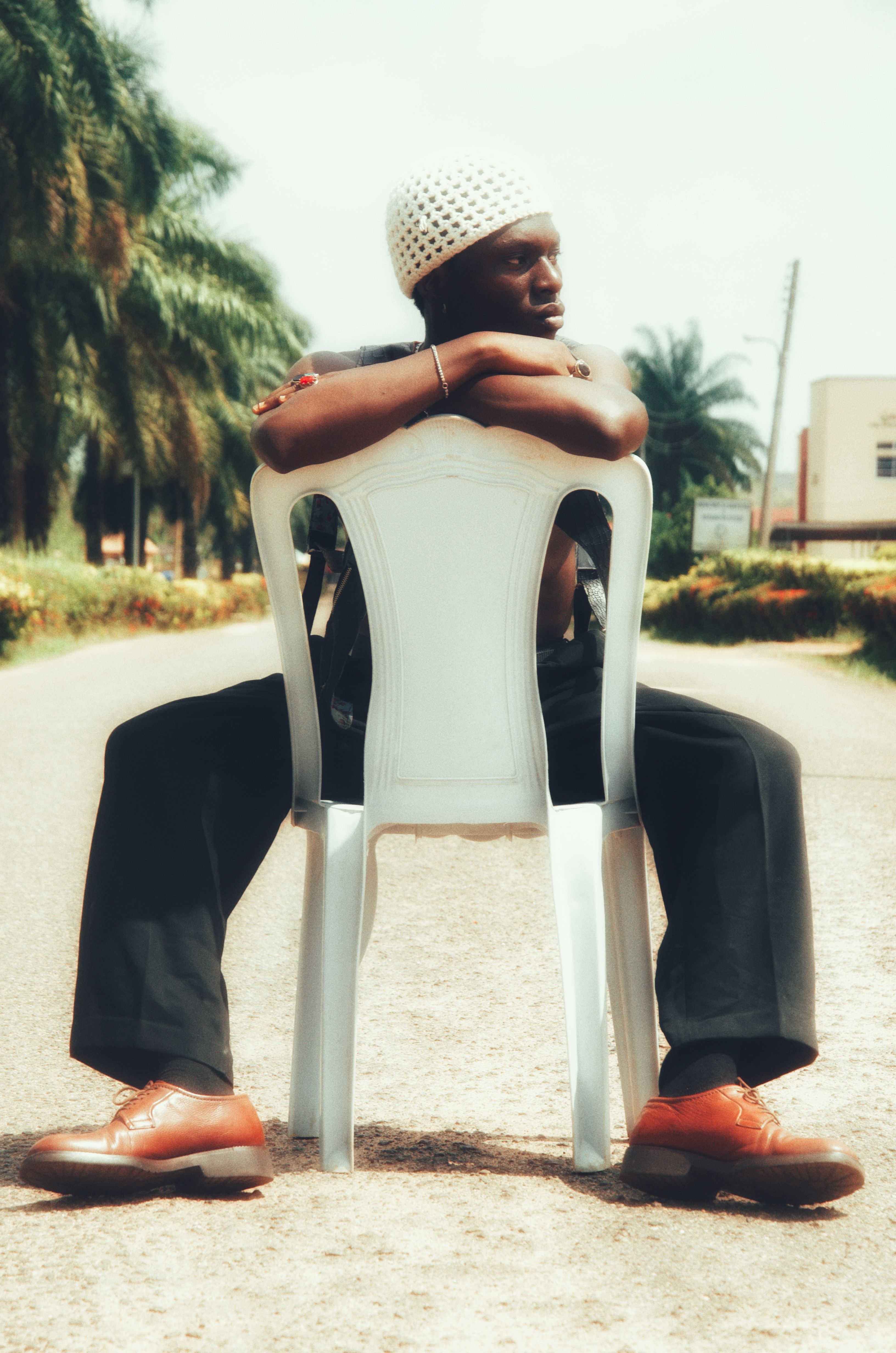 A person sits on a chair in the middle of a palm-lined street, exuding a relaxed vibe.