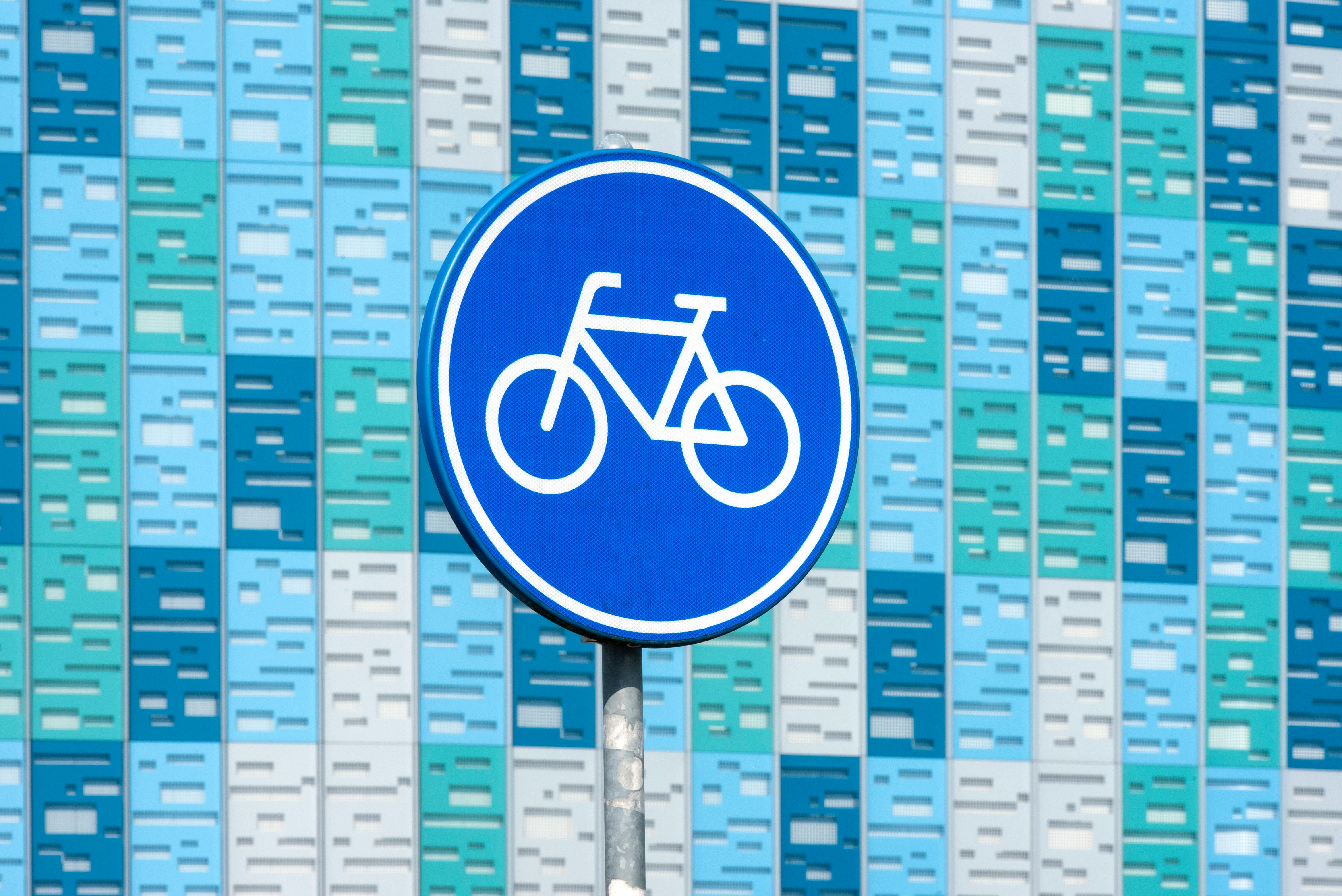 Kostenlos Ein leuchtend blaues Fahrradschild vor einer modernen, geometrischen Fassade in verschiedenen Blautönen. Stock-Foto