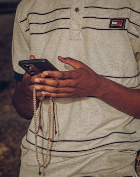 Close-up of individual holding smartphone and beads outdoors.
