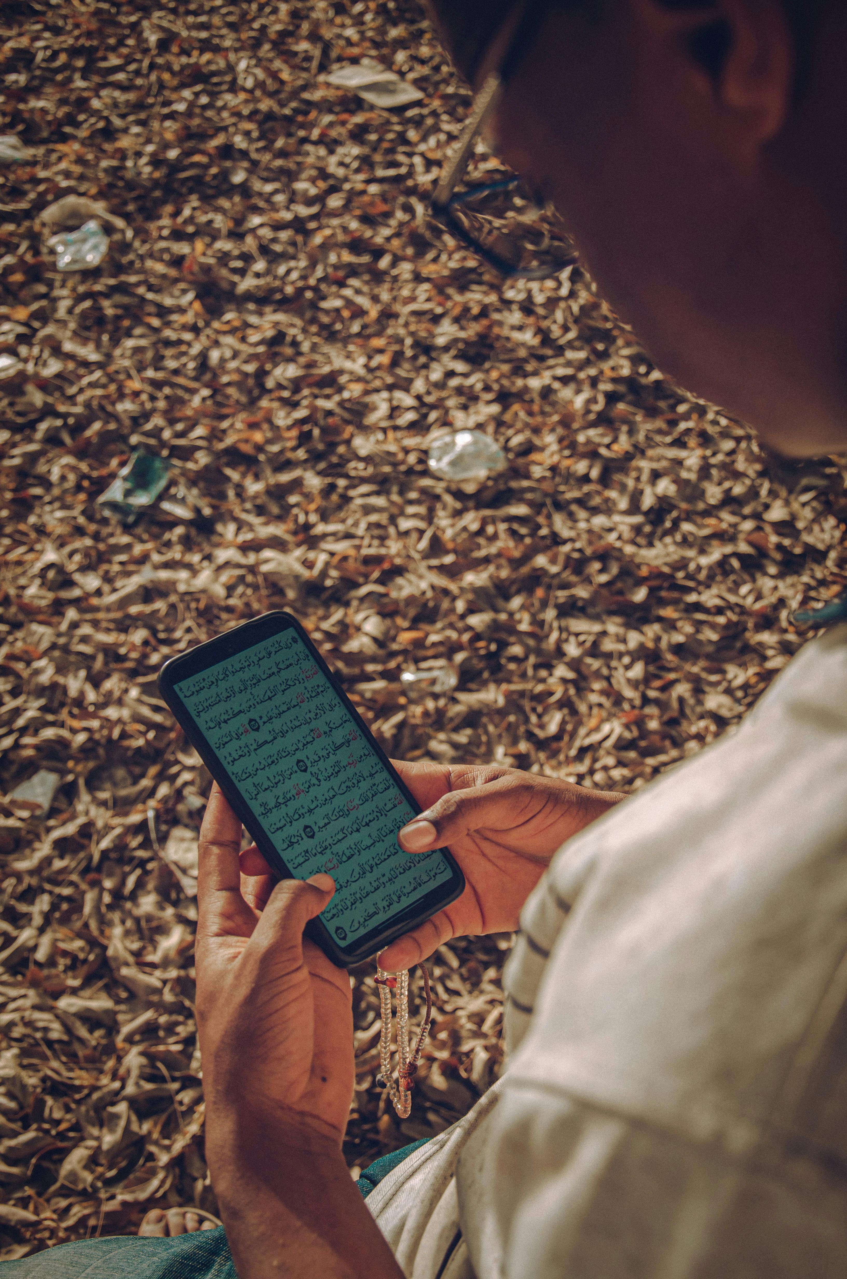 Kostenlos Ein kaukasischer Mann liest im Freien, umgeben von Blättern, auf seinem Handy den Koran. Stock-Foto