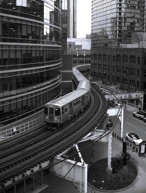 Black and white photo of a Chicago L train navigating a curve in downtown Chicago, Illinois.