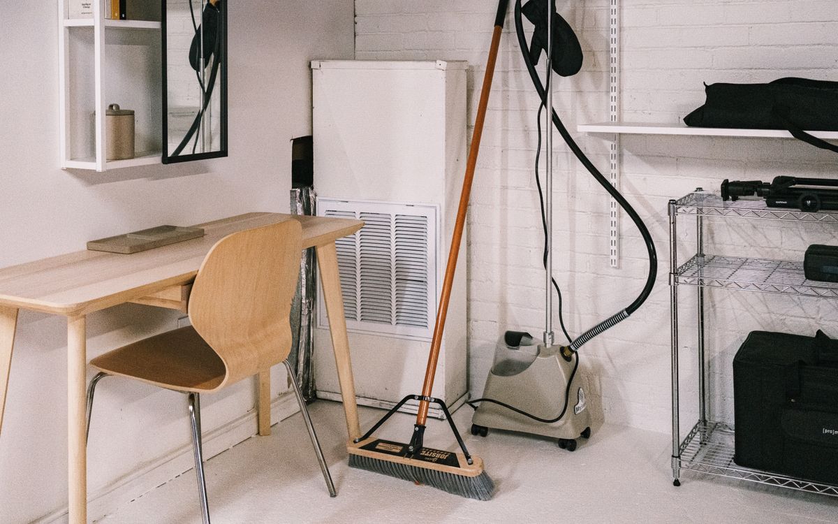A tidy home office space featuring a wooden desk, chair, broom, and cleaning equipment.