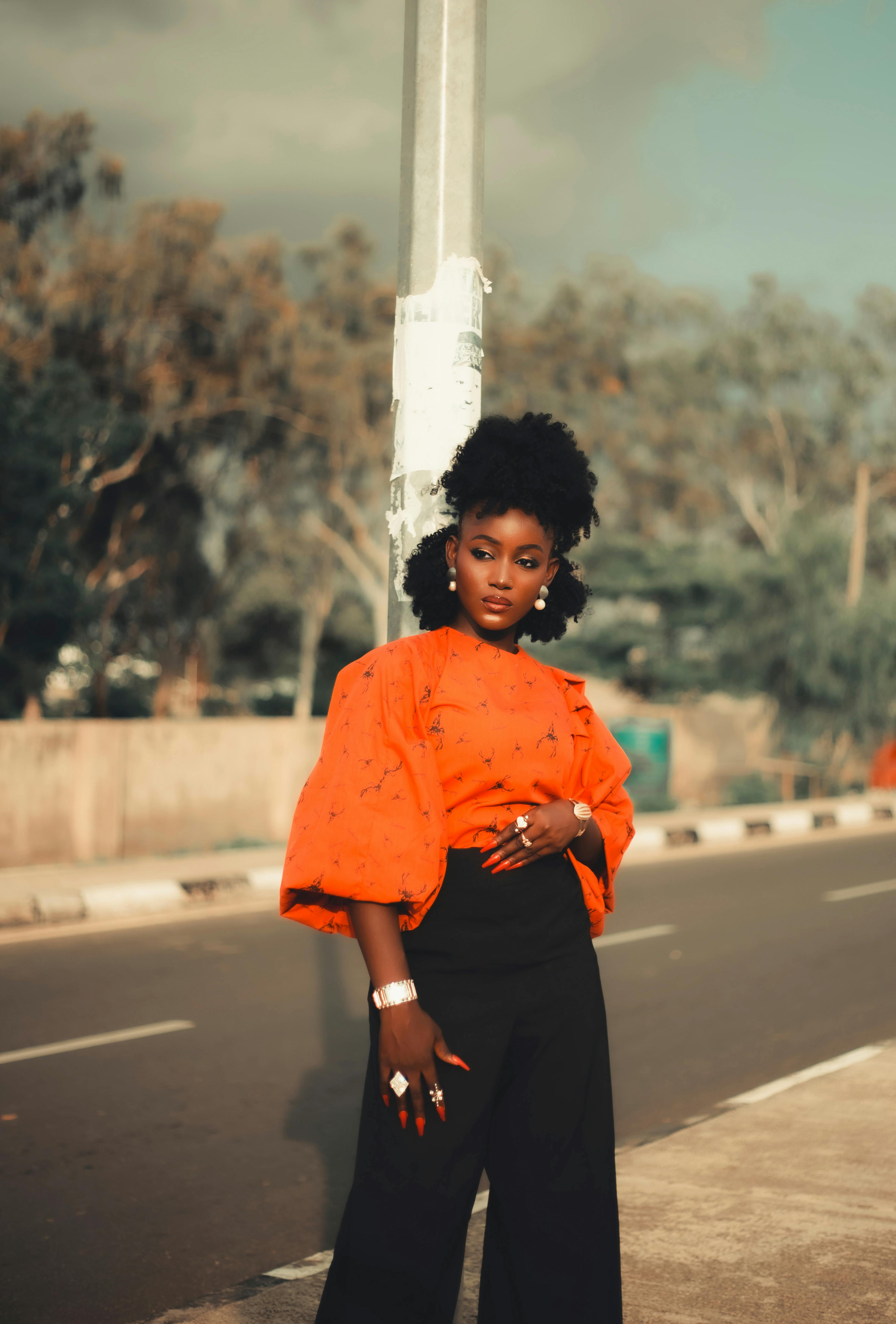 Kostenlos Eine schicke Frau in einer orangefarbenen Bluse steht selbstbewusst auf der Straße und strahlt Stil und Eleganz aus. Stock-Foto