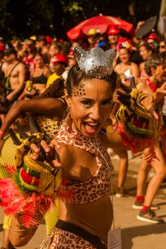 Energetic performer in bright costume at an outdoor carnival parade, showcasing lively expressions and vibrant accessories.