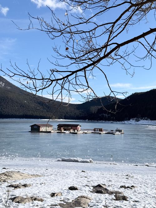 Free Scenic view of frozen lake with floating houses, surrounded by mountains and bare trees. Stock Photo