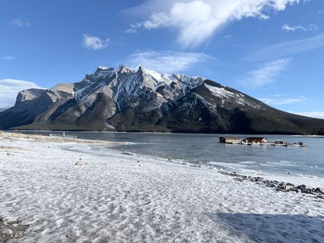 A stunning winter landscape of a frozen lake with majestic mountains and a clear blue sky.