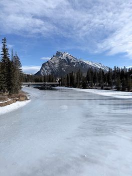 Capture of a frozen river with mountain and trees in Banff National Park. Clear blue sky, winter landscape.