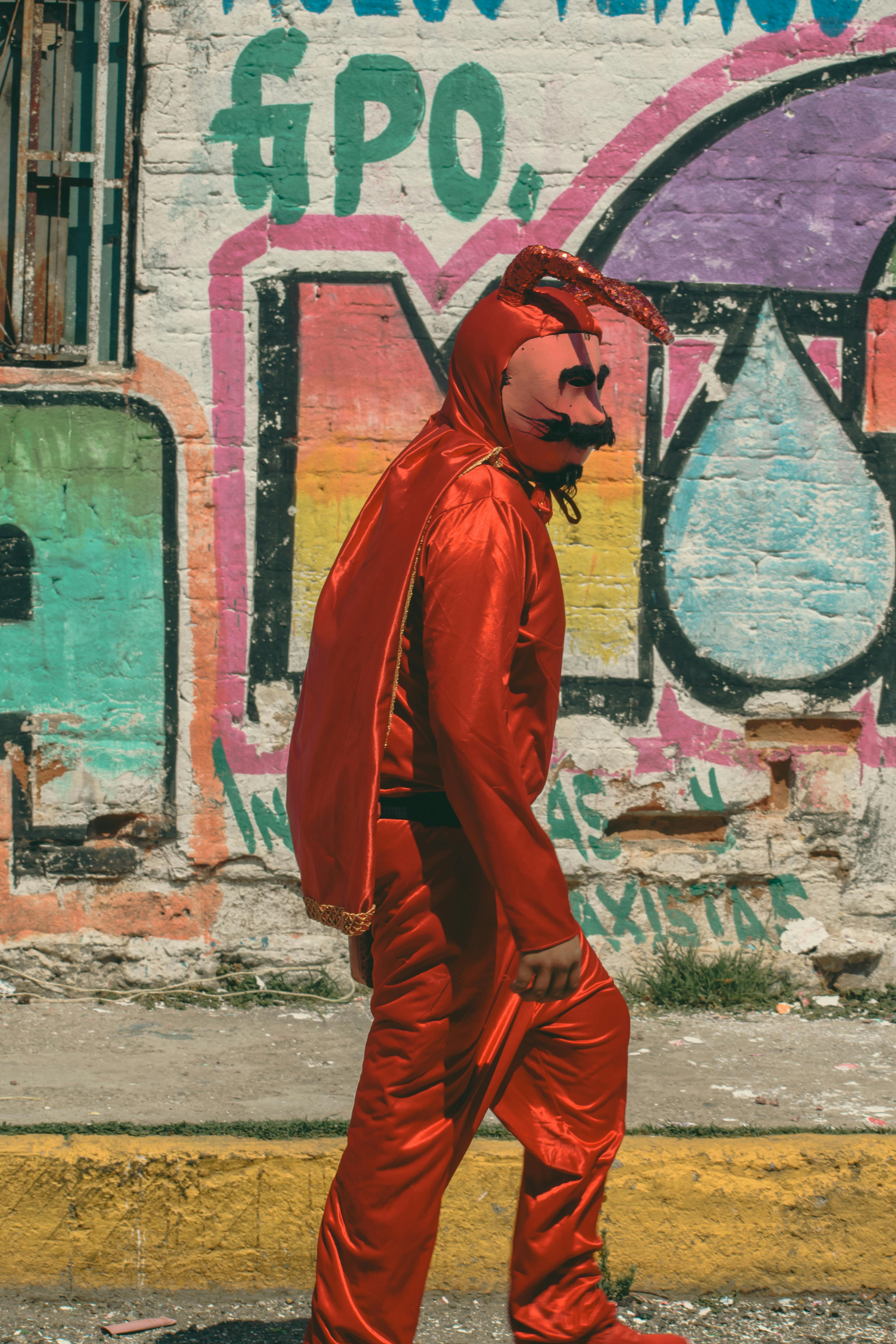 Δωρεάν Ένα άτομο με στολή κόκκινου διαβόλου περπατάει δίπλα σε πολύχρωμα γκράφιτι στην Πατσούκα ντε Σότο του Μεξικού. Φωτογραφία από στοκ φωτογραφιών