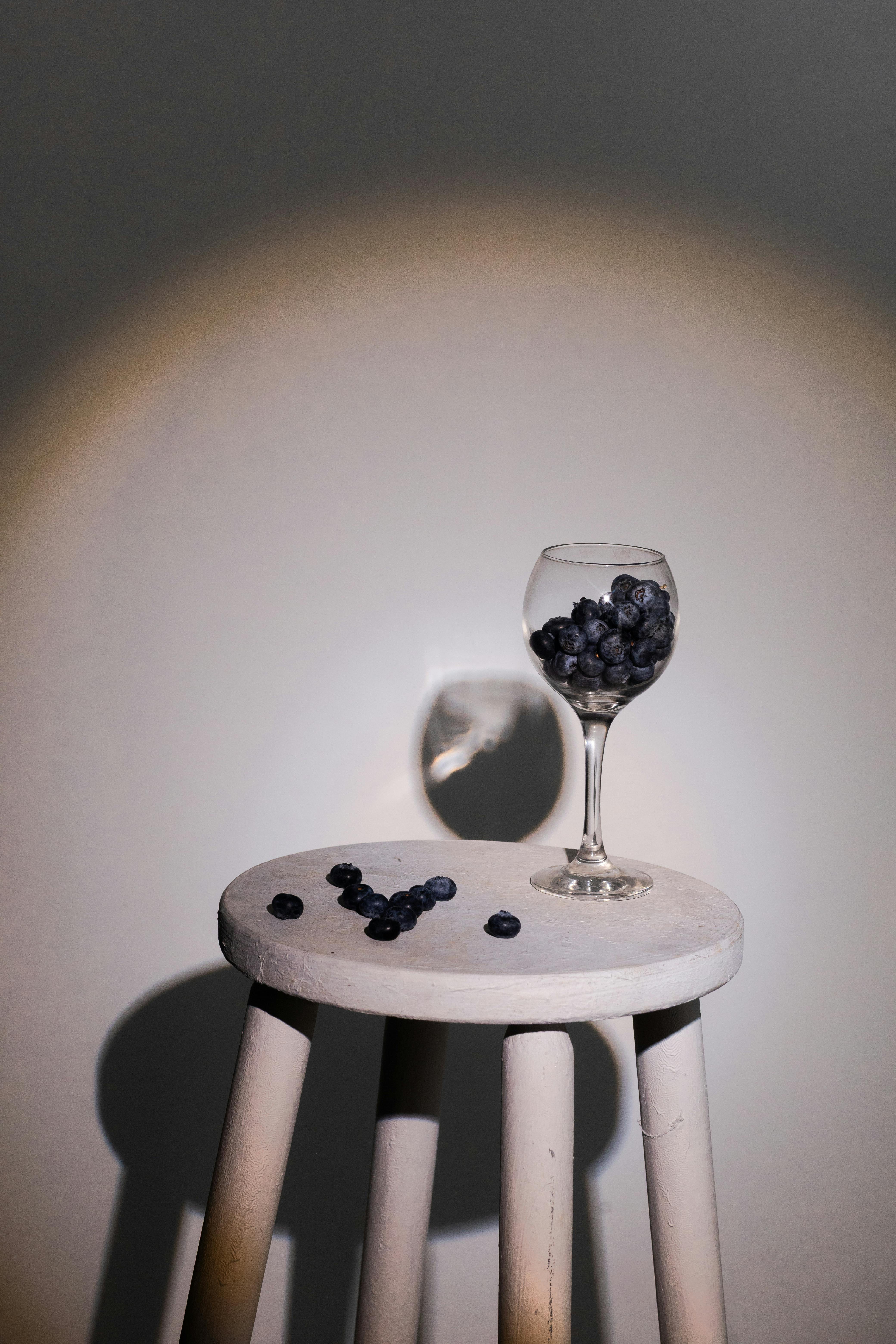 Gratis Kunstnerisk komposisjon med et vinglass med blåbær som kaster en skygge på en krakk. Arkivbilde