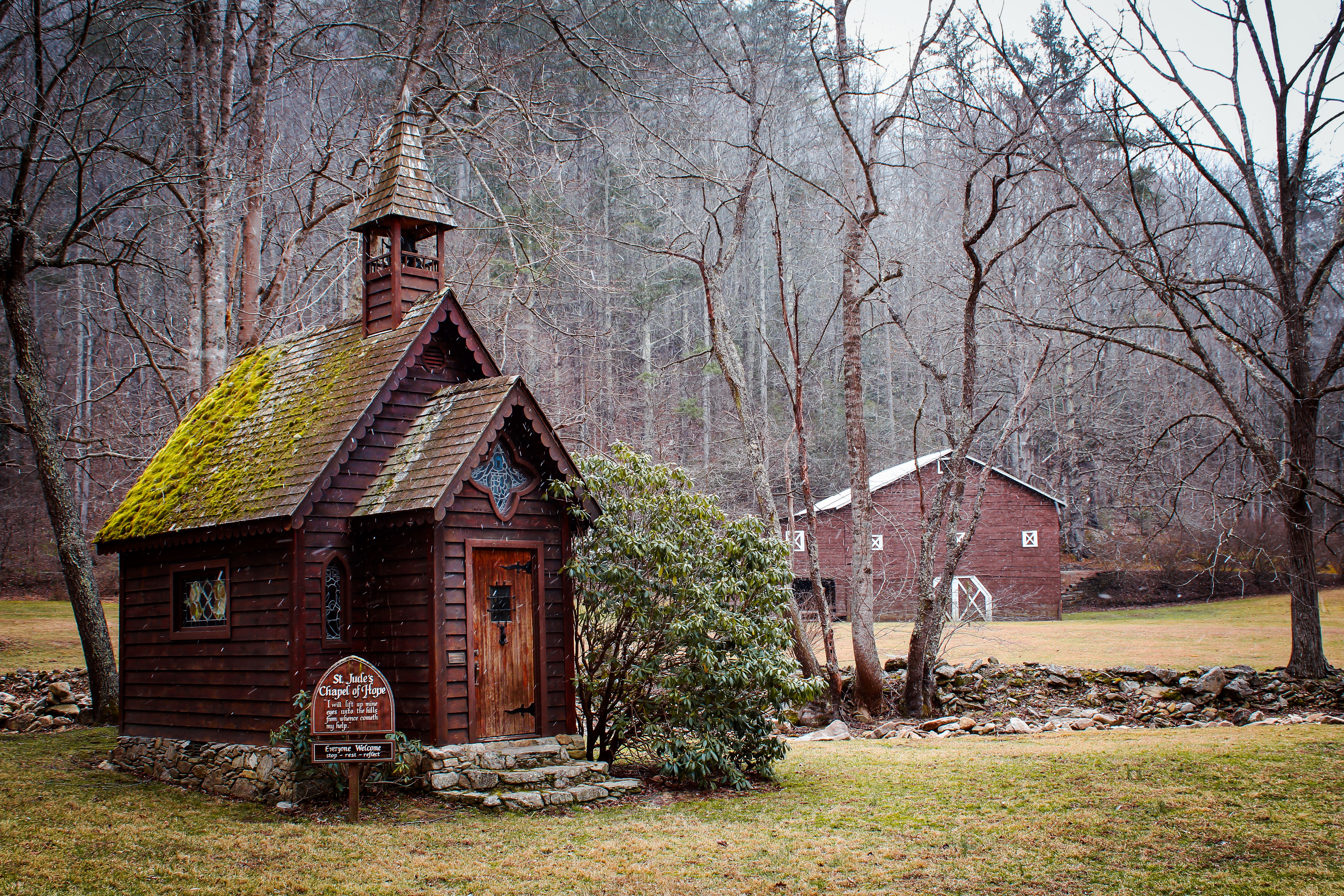 Charming wooden chapel with moss-covered roof in a tranquil forest during winter.