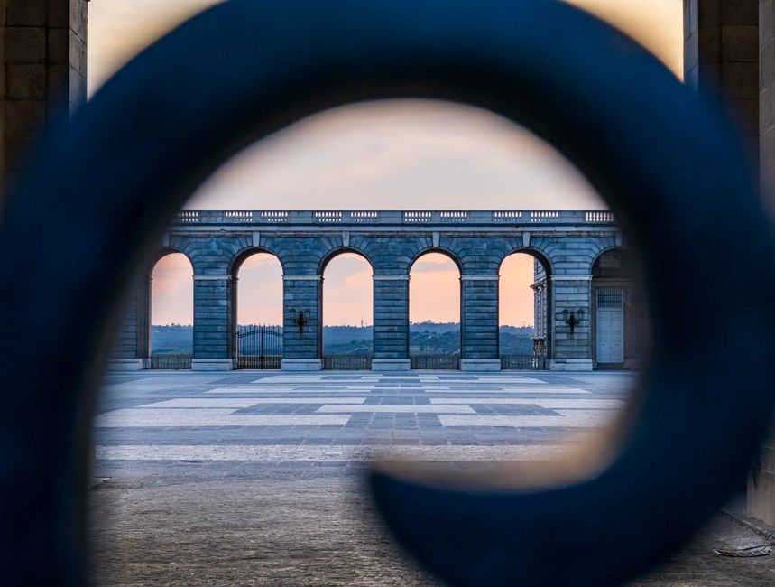 Beautiful view through ornate ironwork towards historic archway at sunset.
