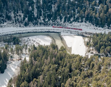 A red train travels through a snowy forest landscape captured from above, highlighting winter's beauty.