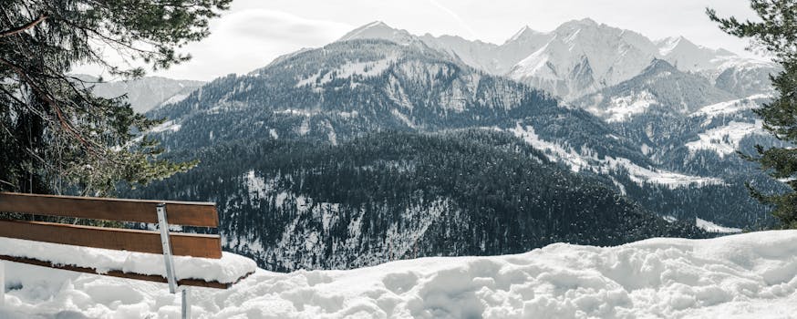 A tranquil winter view of snowy mountains with a bench in the foreground, perfect for nature lovers.