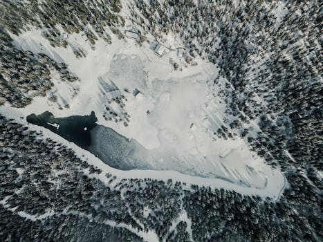 Aerial view of a snowy forest surrounding a frozen lake, showcasing winter tranquility.