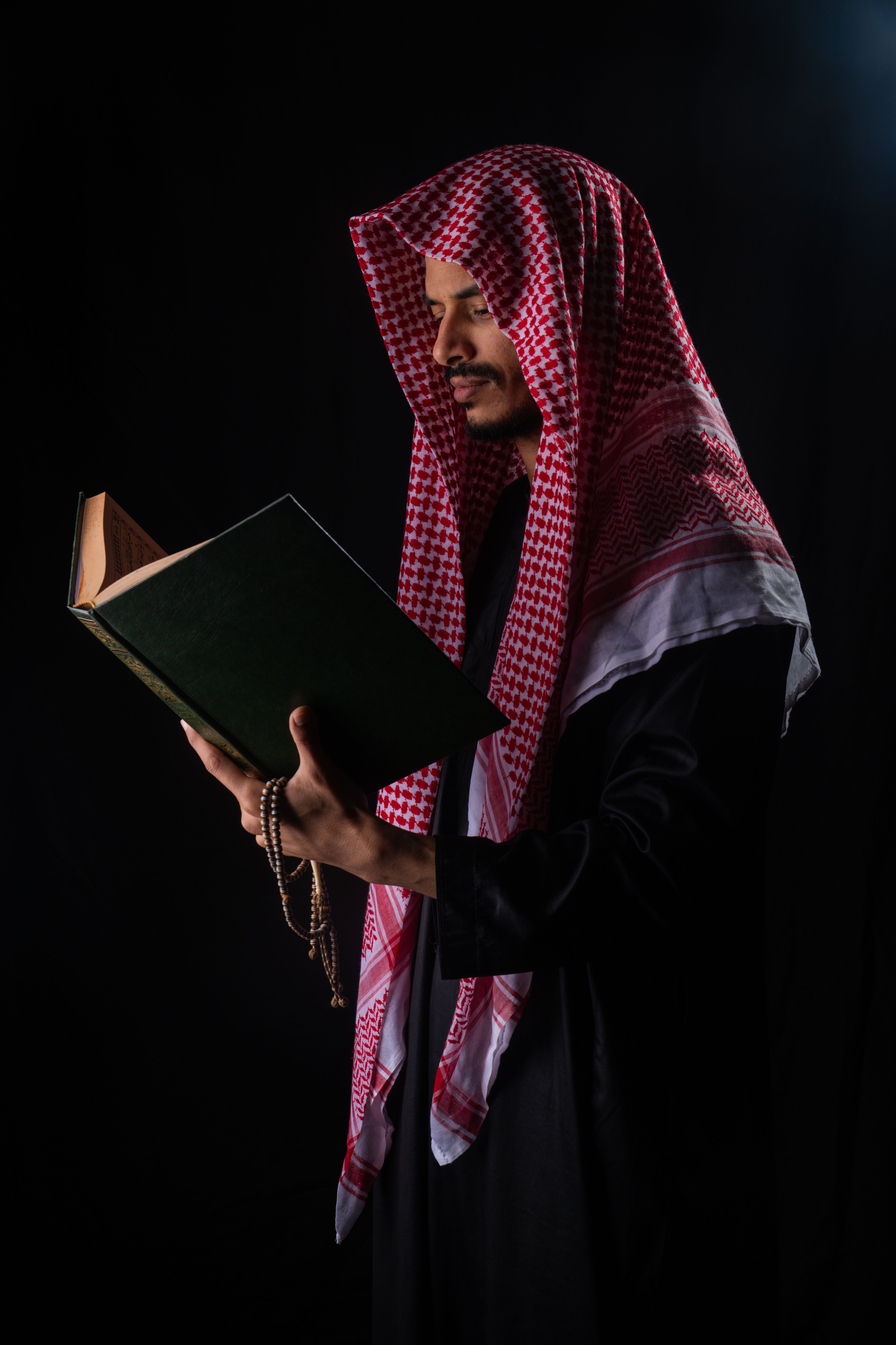Man in traditional attire reading a book against a dark background.