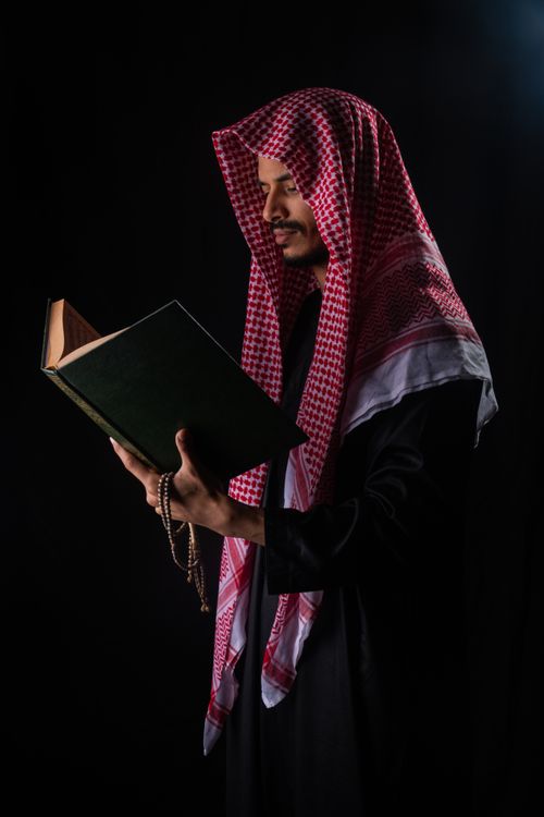 Free Man in traditional attire reading a book against a dark background. Stock Photo