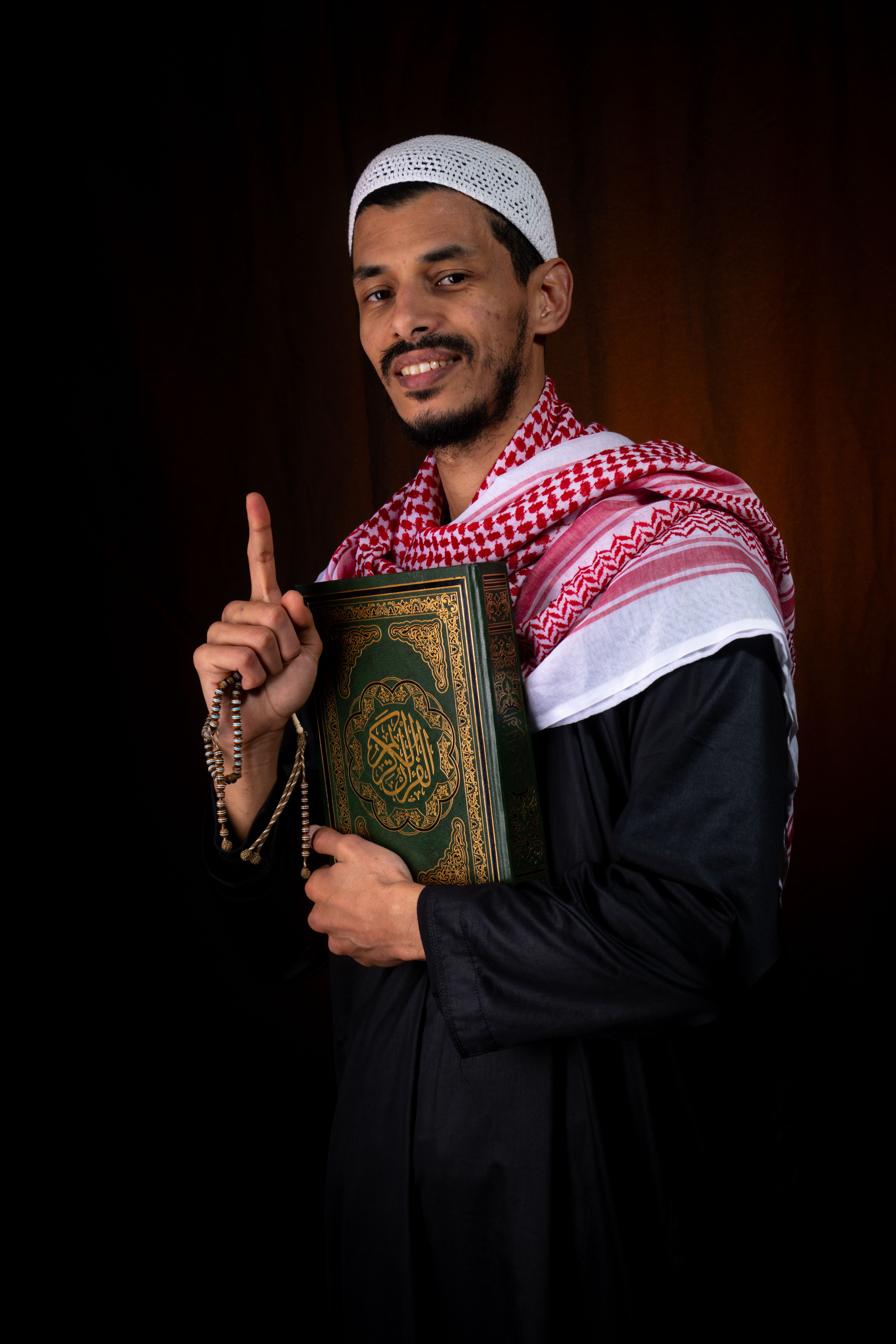 Religious Muslim man in traditional attire holding Quran, displaying faith and spirituality.
