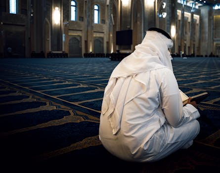A man dressed in traditional clothing praying inside a grand mosque in Kuwait City, offering a serene atmosphere.