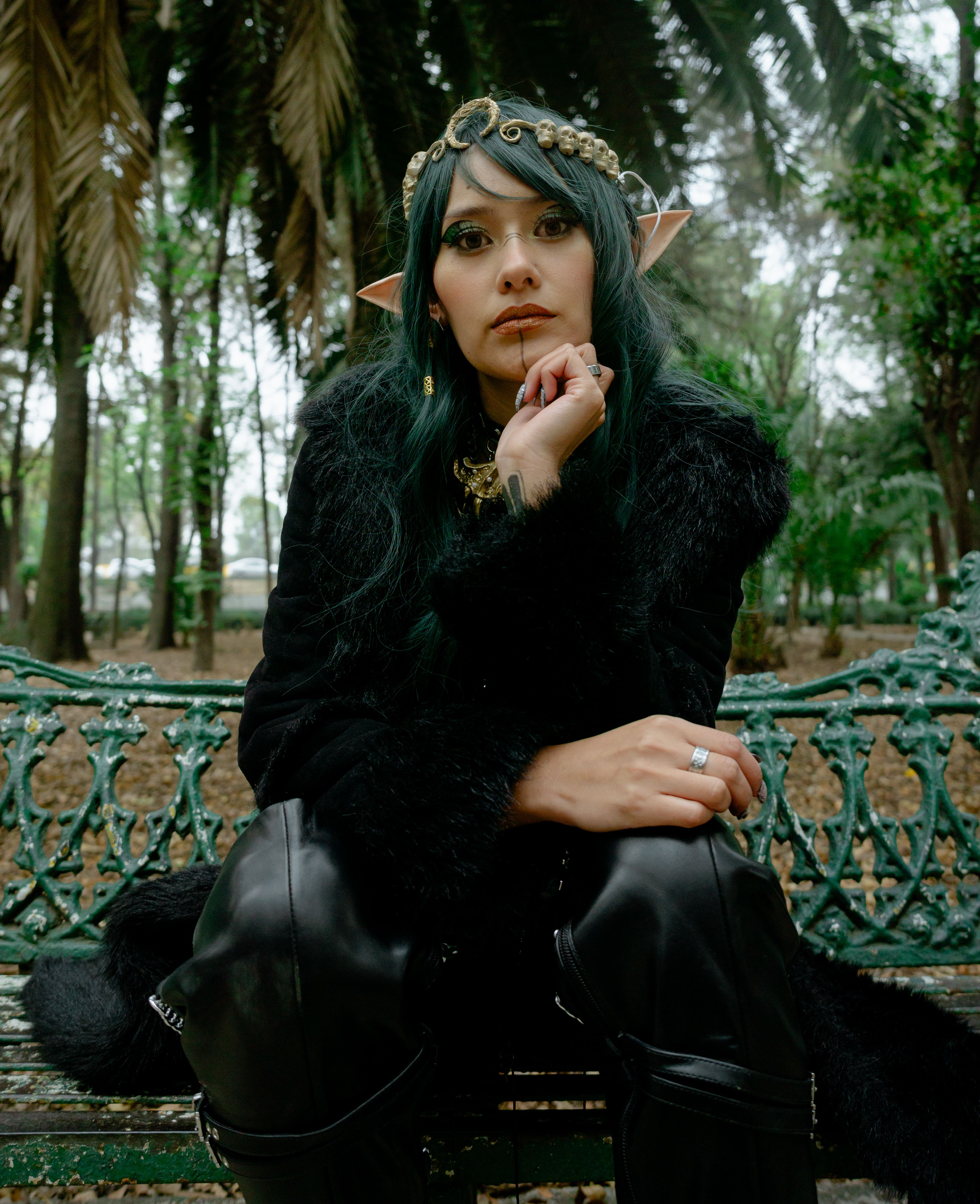 A woman dressed in fantasy attire sits on a bench in a wooded area, exuding a mystical vibe.