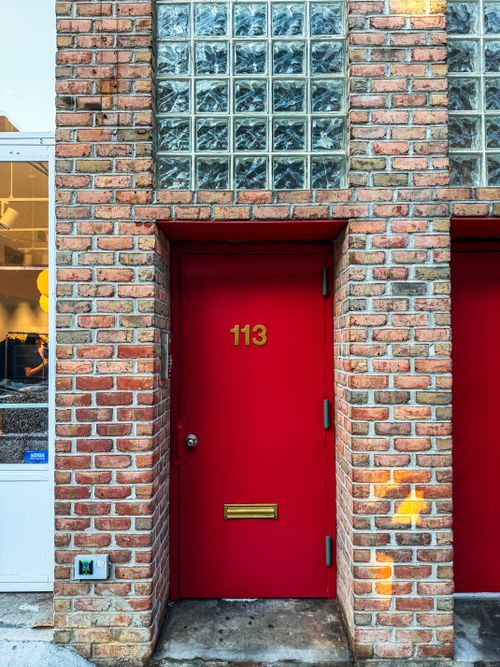 Free Bright red door with number 113 on a textured brick wall, New York street. Stock Photo