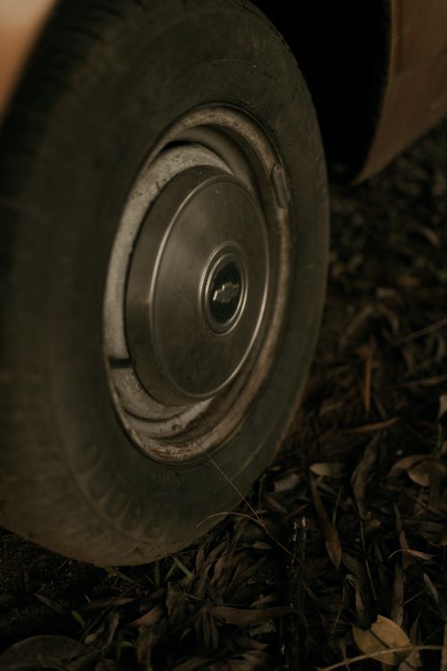 Free Detailed view of a vintage car wheel surrounded by fallen leaves on the ground. Moody and nostalgic atmosphere. Stock Photo
