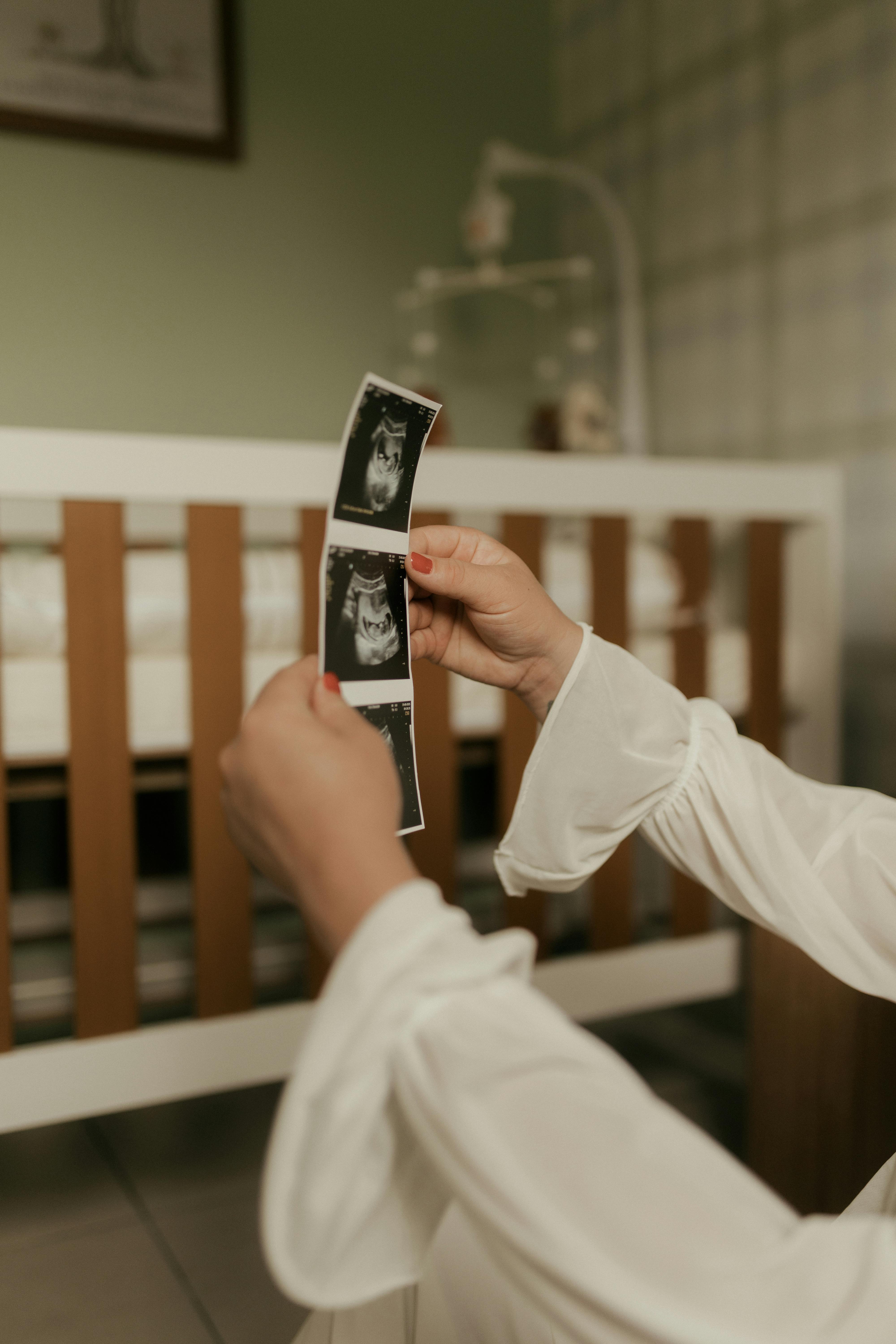 Free A woman in a nursery holding ultrasound photos, symbolizing anticipation and motherhood. Stock Photo
