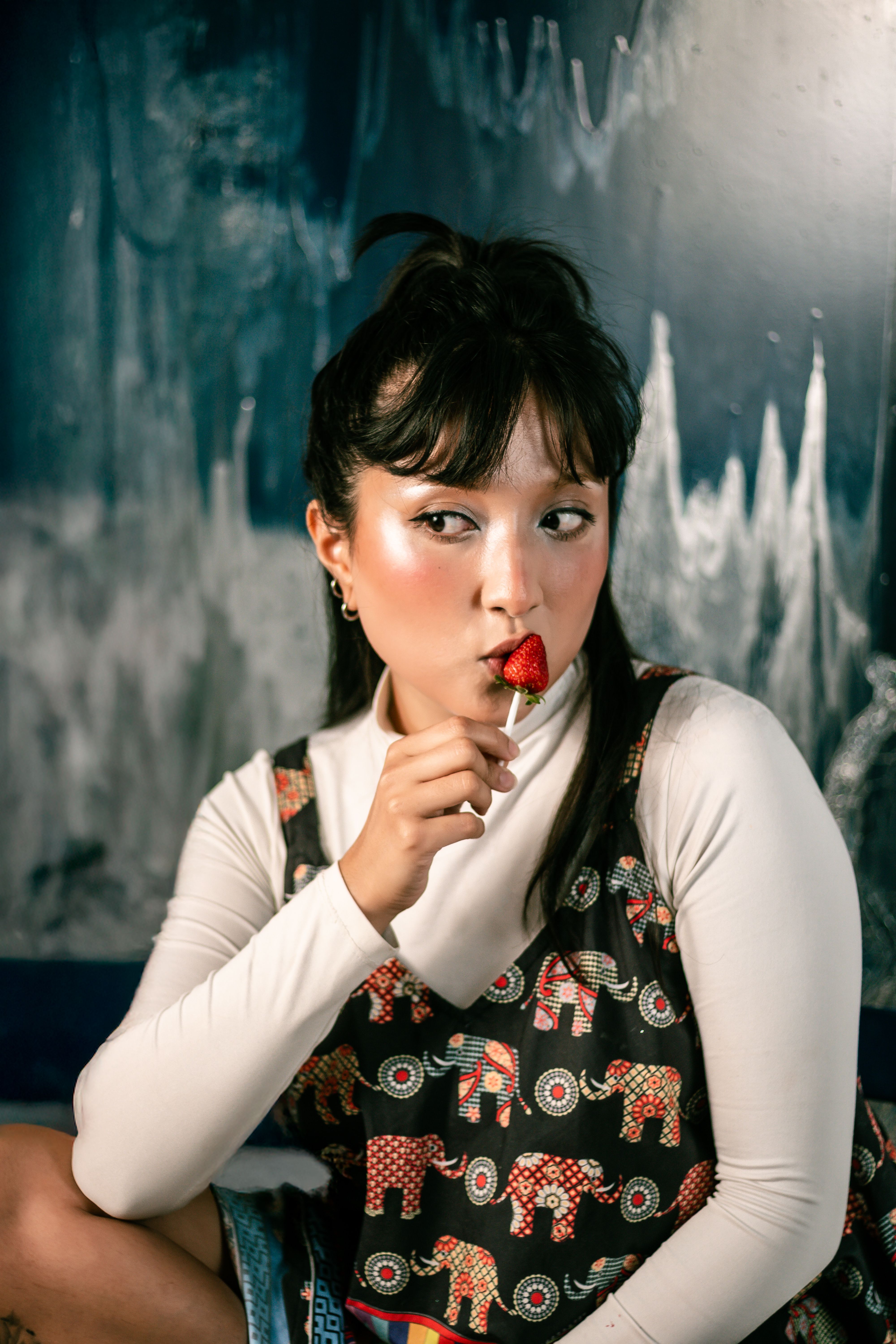 Portrait of a young woman savoring a strawberry lollipop against a dark abstract background in São Paulo.