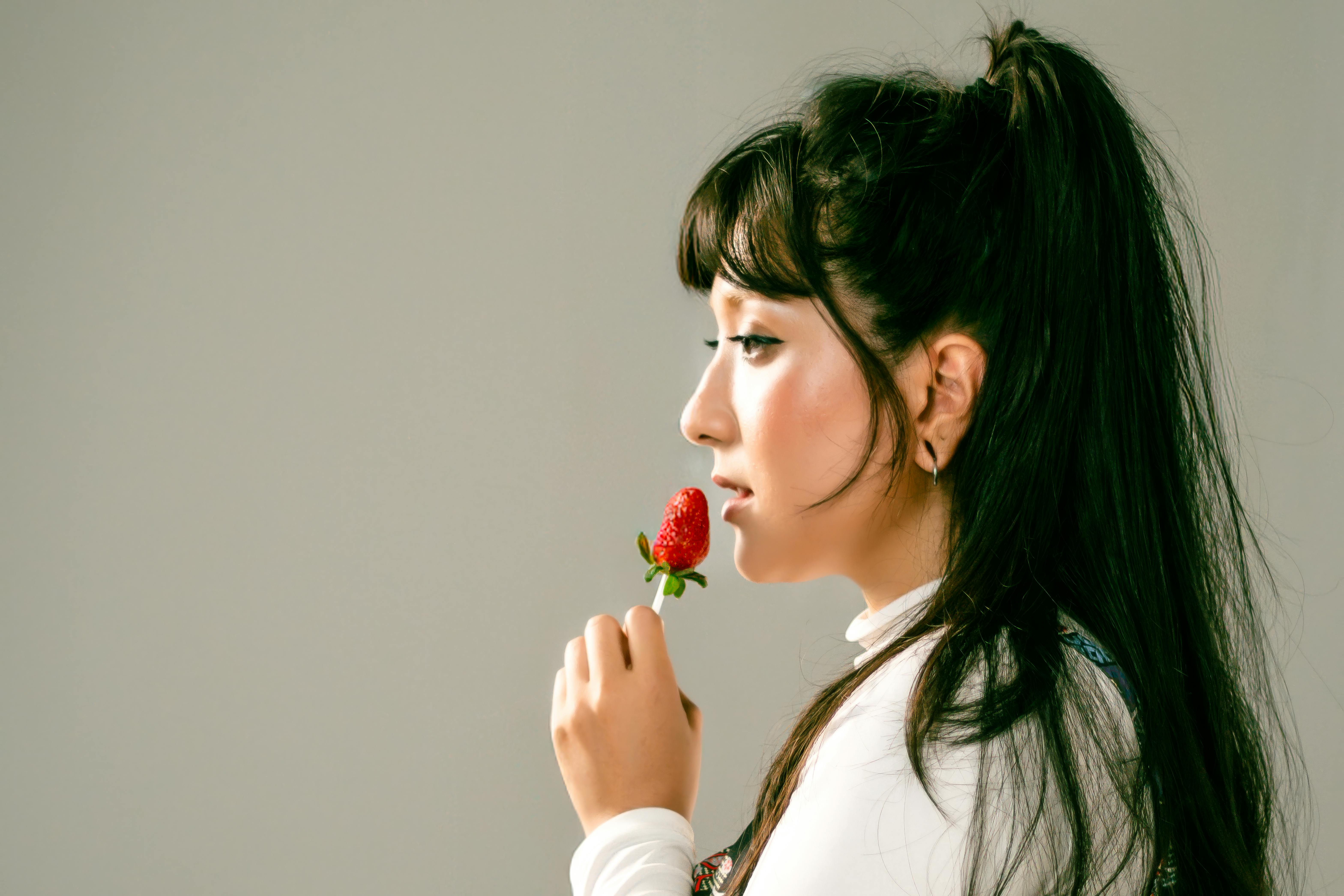 Free Side profile of a woman holding a strawberry with a contemplative expression. Stock Photo