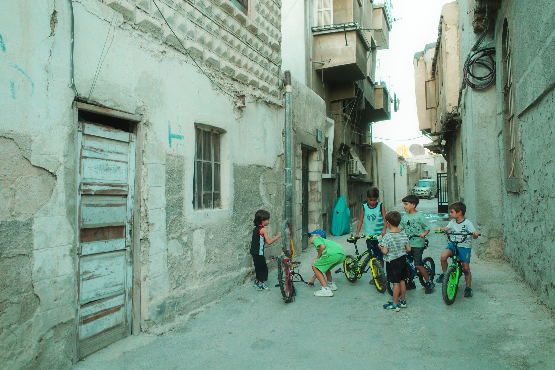 A group of children gather with bicycles in a narrow alleyway in Damascus, Syria, creating a lively neighborhood scene.