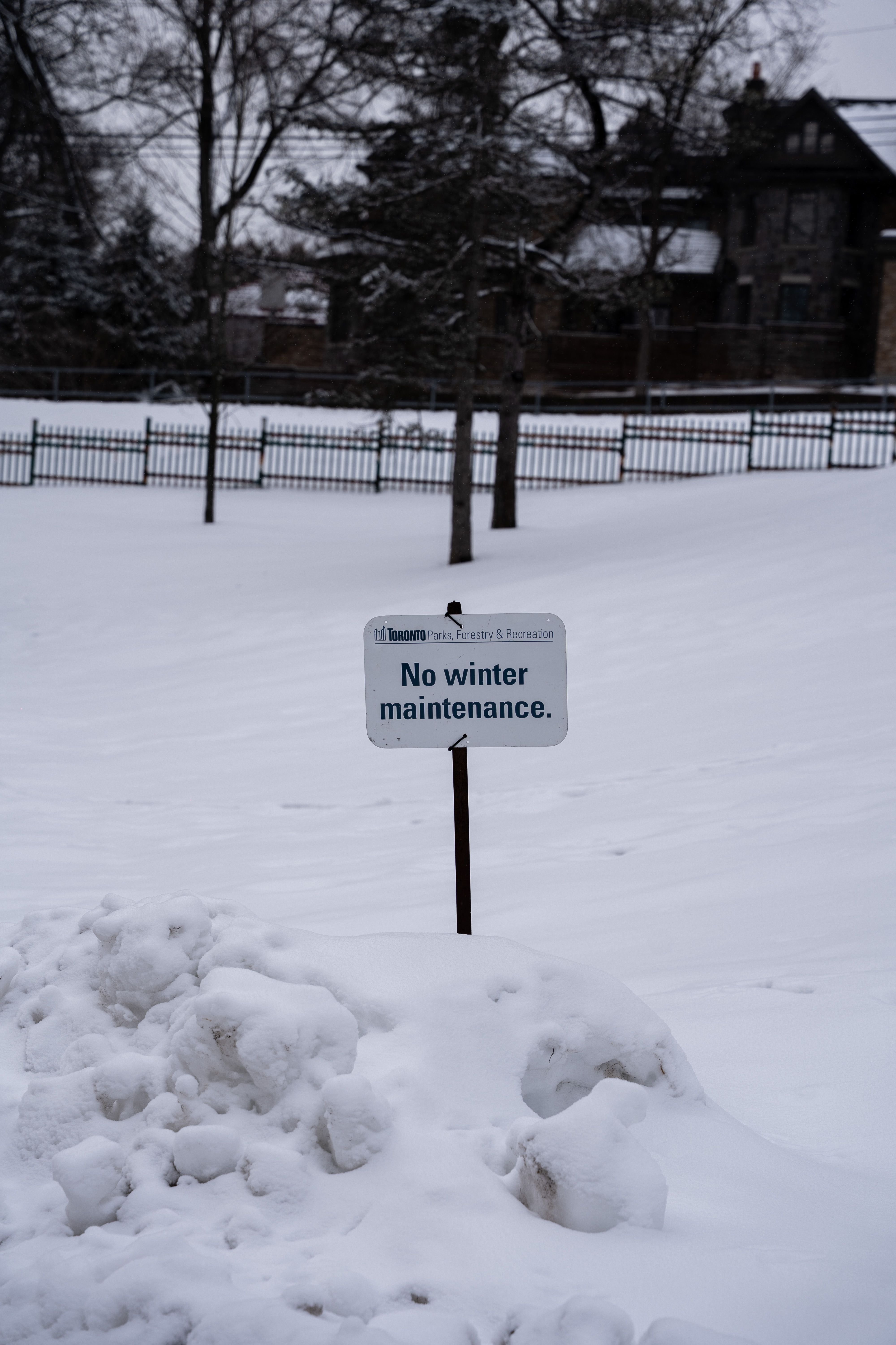 A snowy park with a sign indicating no winter maintenance, highlighting winter safety.