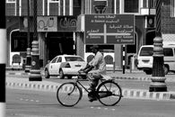 Cyclist in Salalah, Oman amidst bilingual road signs, capturing daily life and cultural heritage.