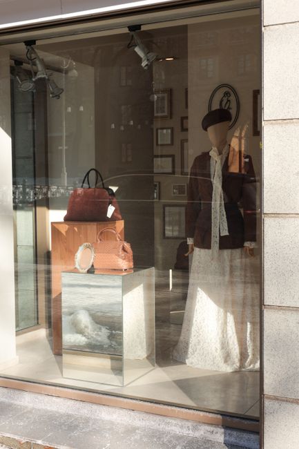 Elegant storefront display featuring a mannequin, leather handbags, and fashion accessories.